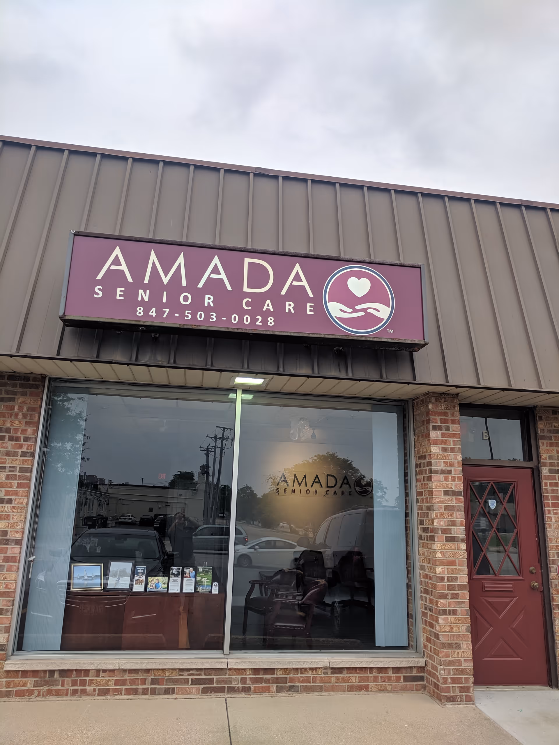 The storefront of Amada Senior Care features a purple sign and large glass windows.