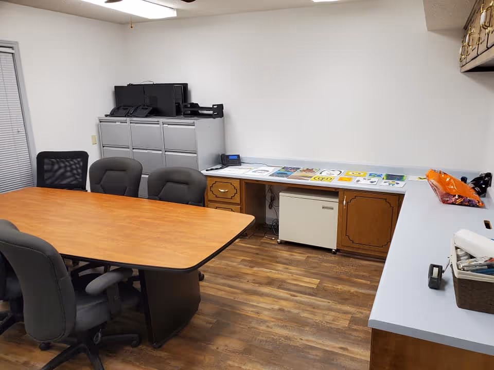A conference-style room with a wooden table, chairs, and file cabinets along the wall.