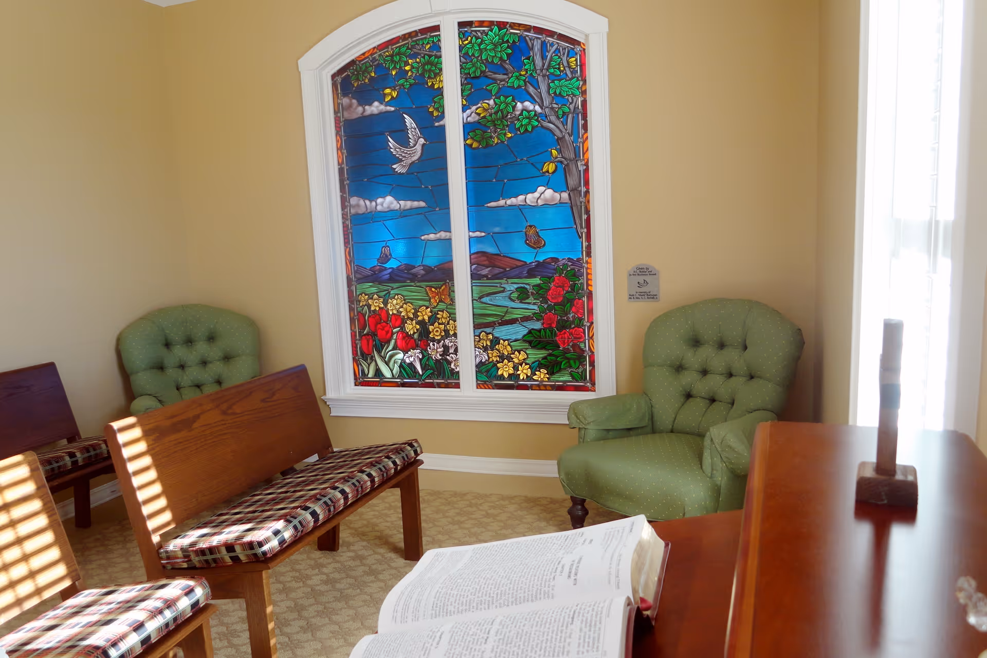 Interior room with stained glass window, green armchairs, wooden benches, and an open book.