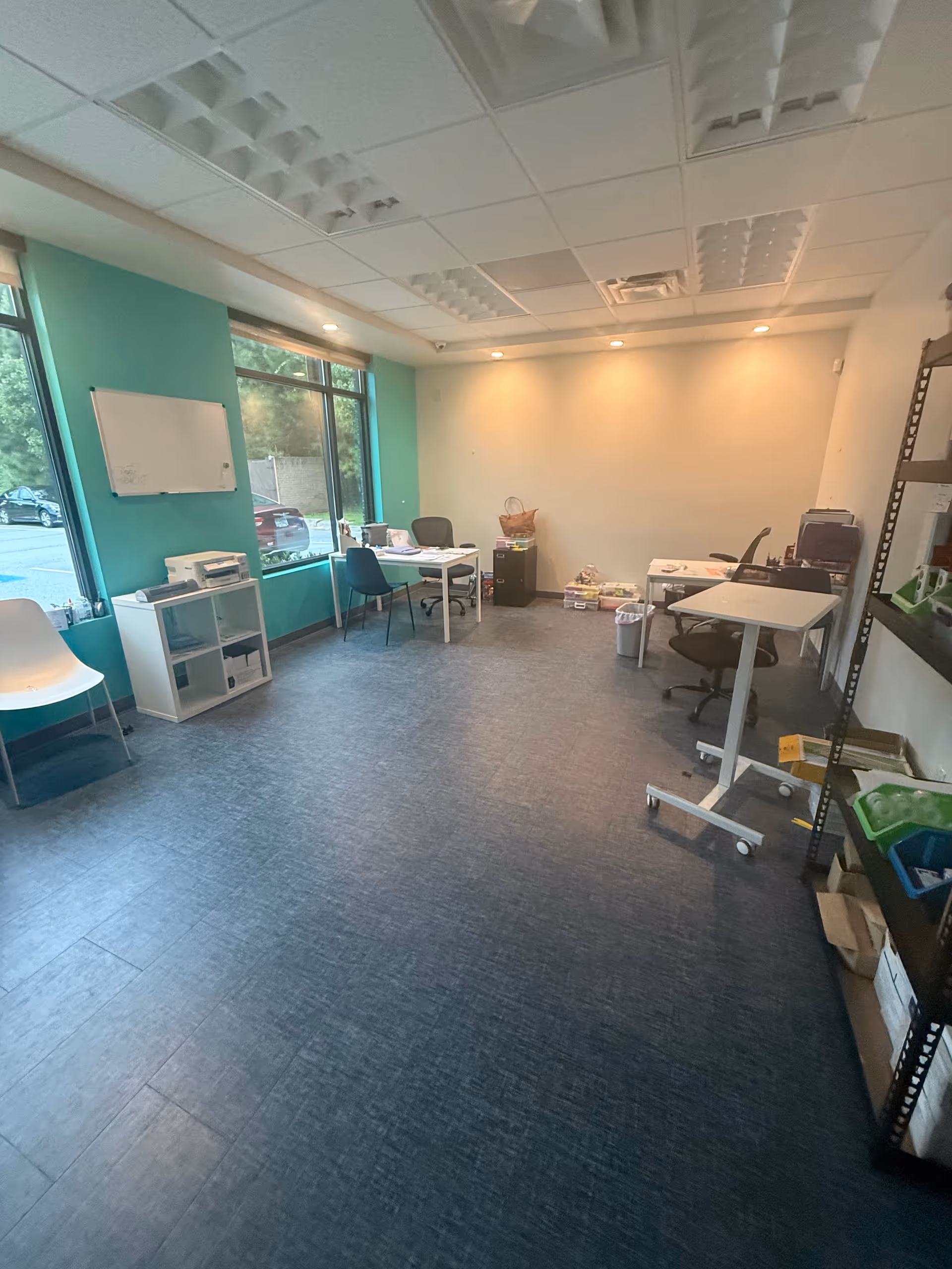 Empty therapy room with tables, chairs, a whiteboard, and teal wall.