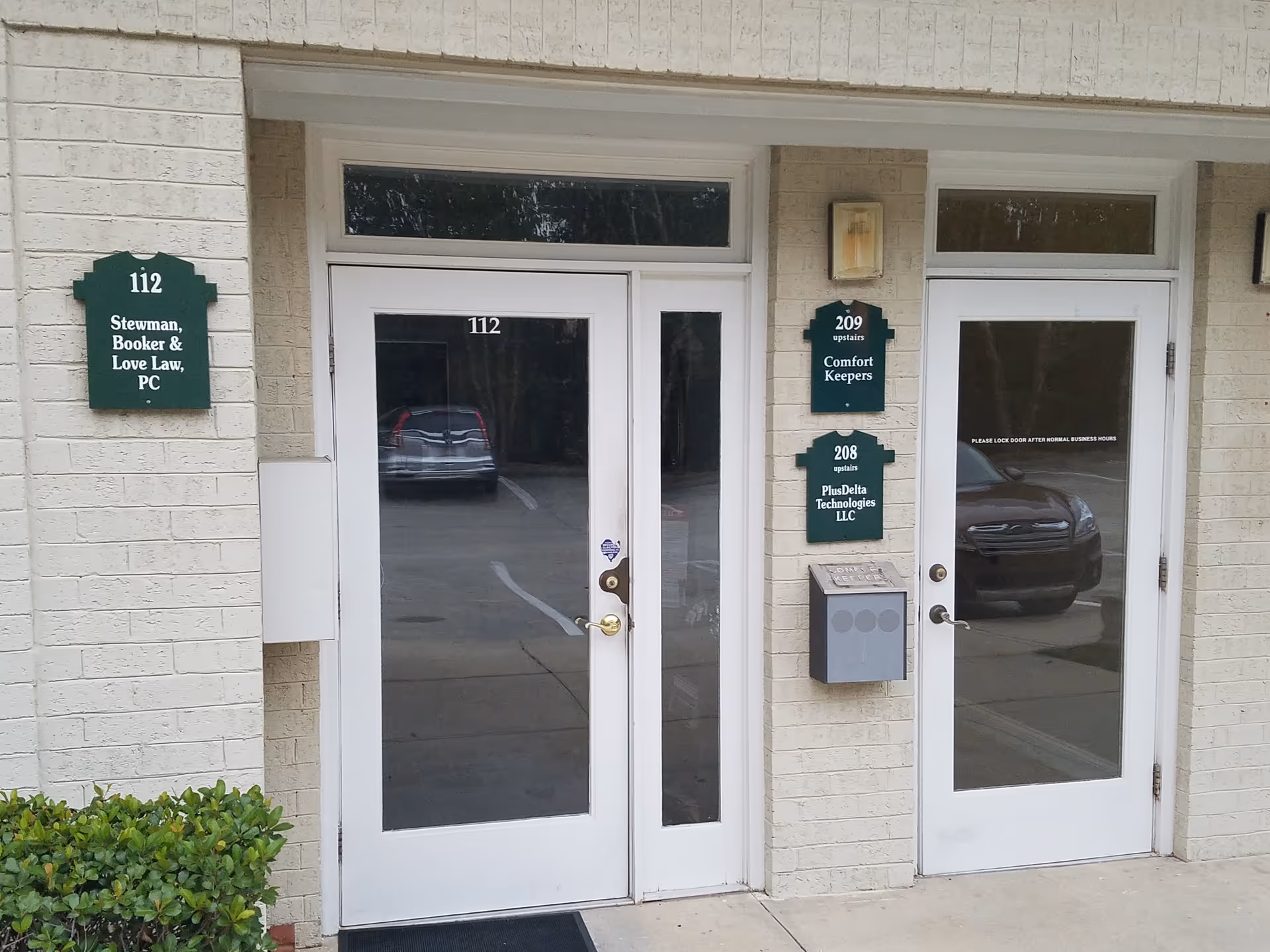 Exterior entry of Comfort Keepers facility with glass doors, address plaques, and a parked car reflection.