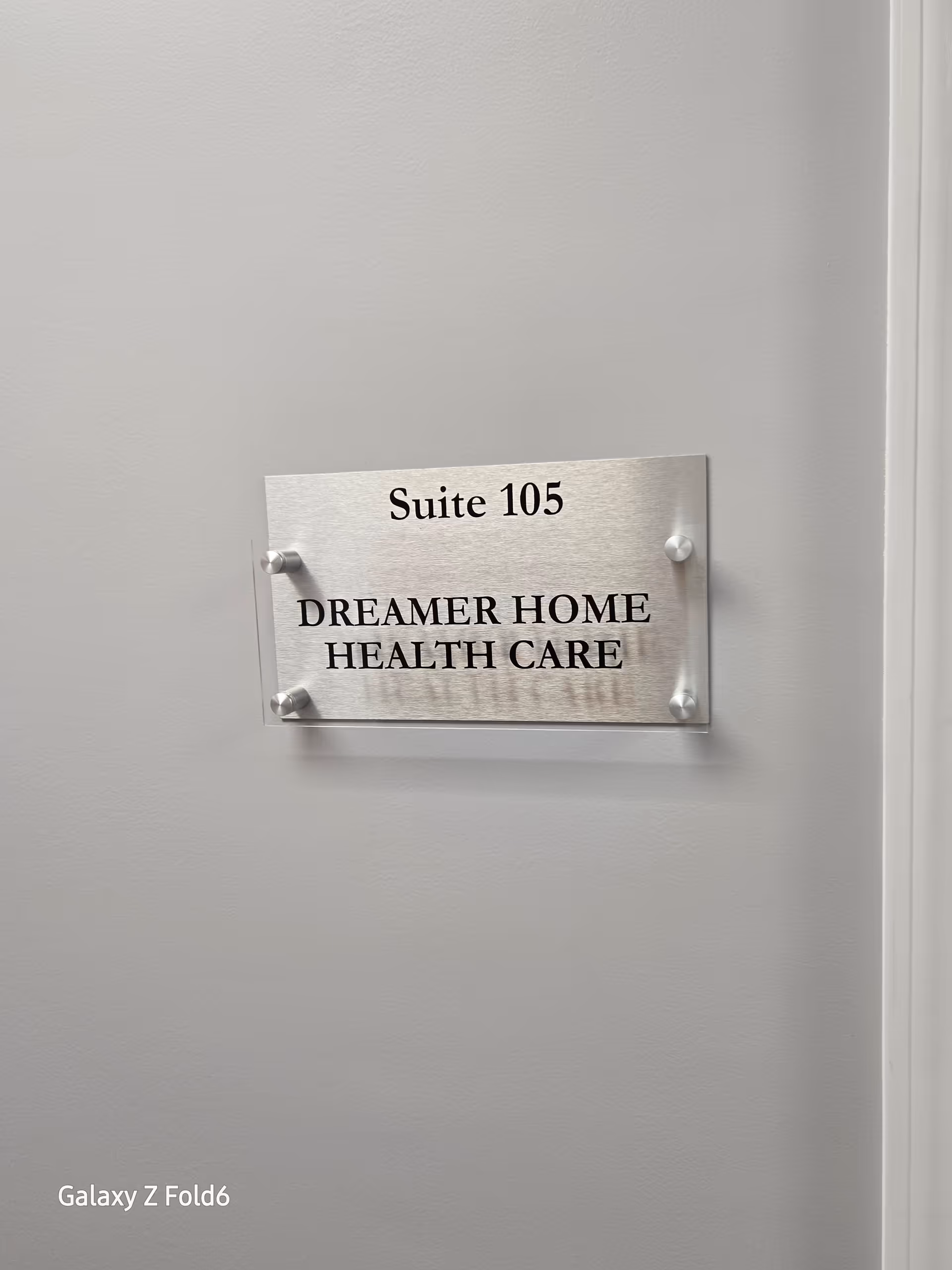 Metal plaque on a plain wall reads Suite 105 Dreamer Home Health Care.