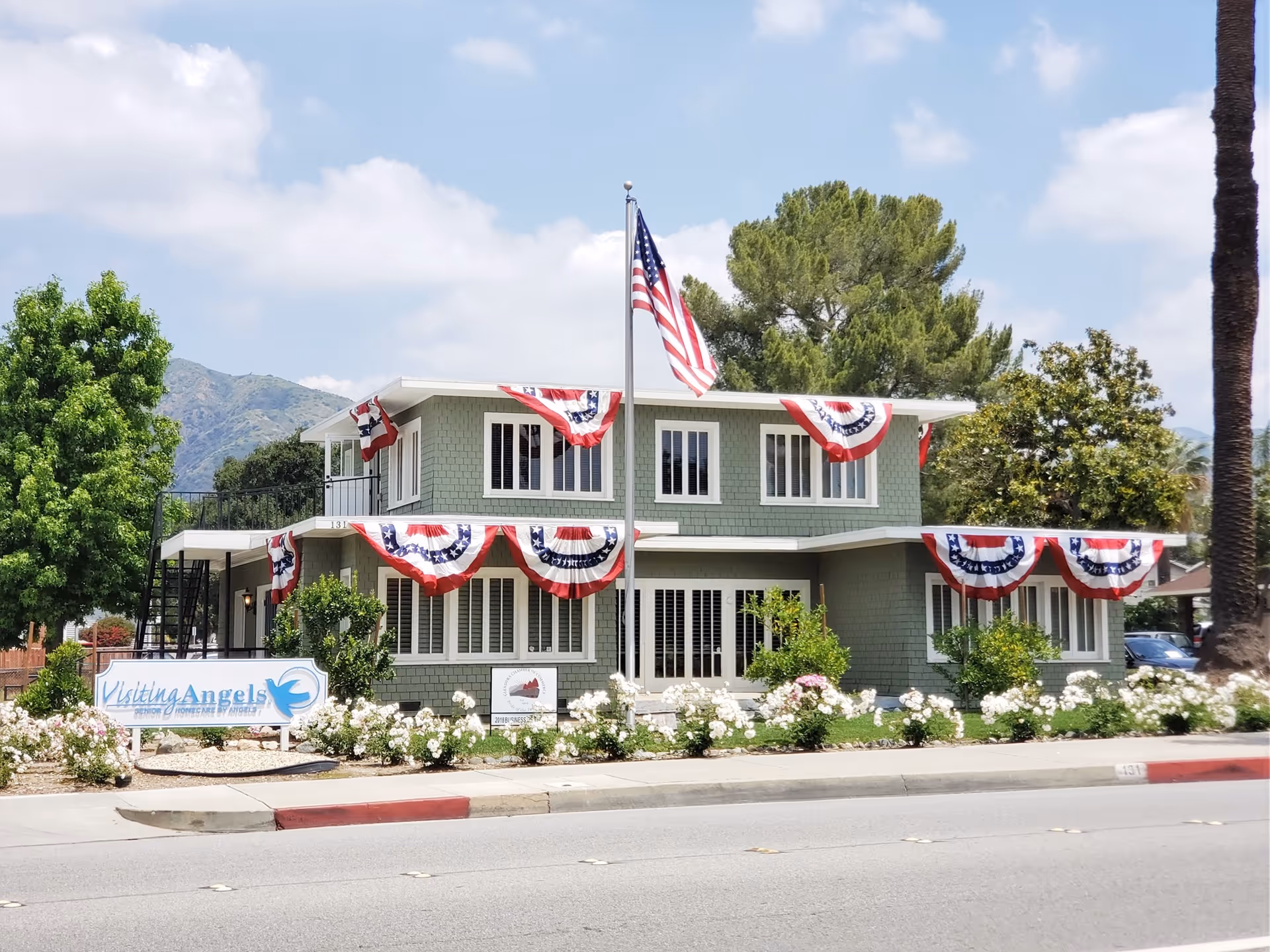 Green two-story senior home care building with Visiting Angels sign and patriotic bunting.