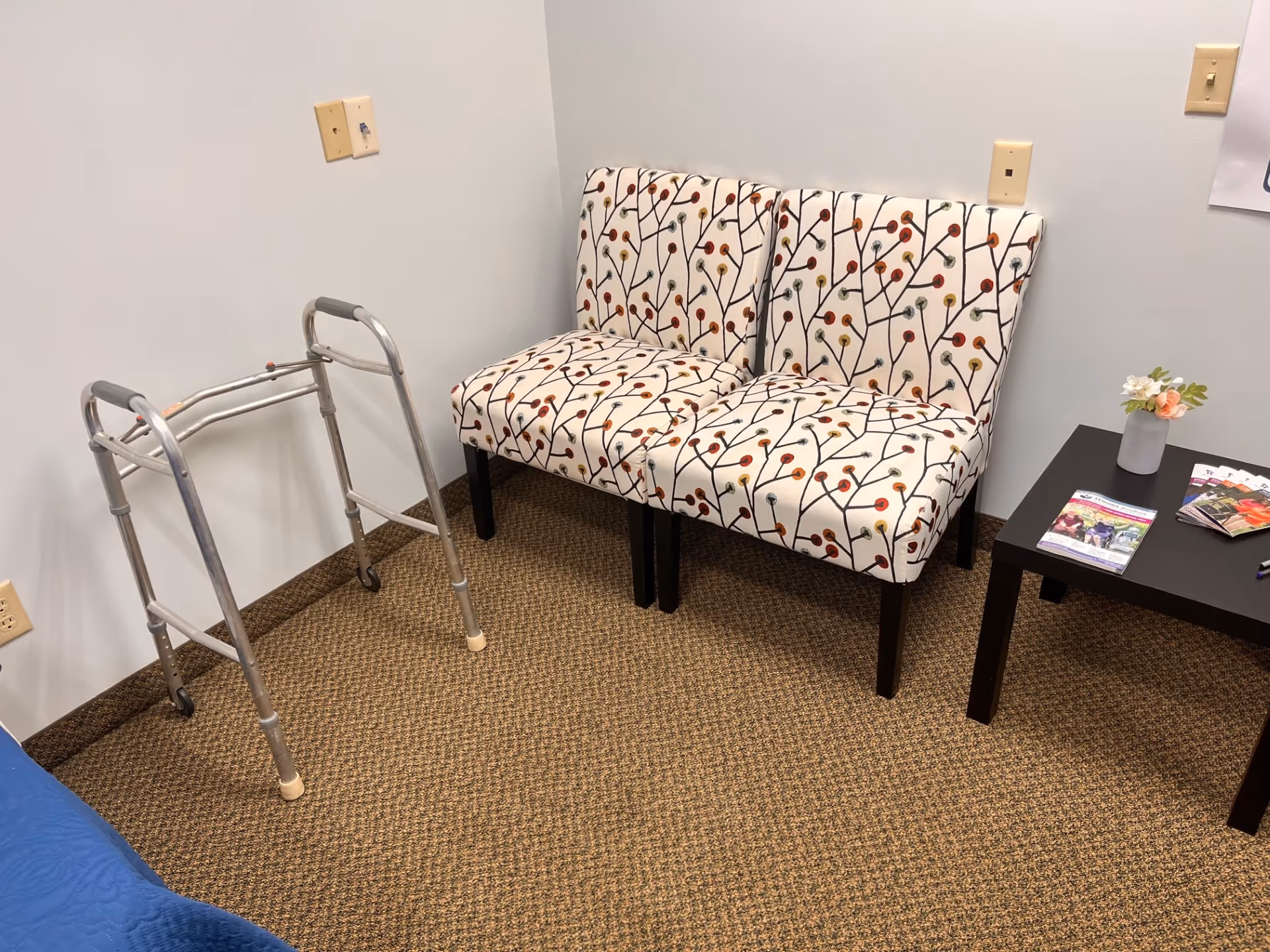 A Senior Helpers facility lounge with patterned chairs, a walker, and a magazine table.
