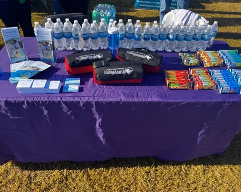 Outdoor table with bottled water, snacks, and brochures on a purple tablecloth.