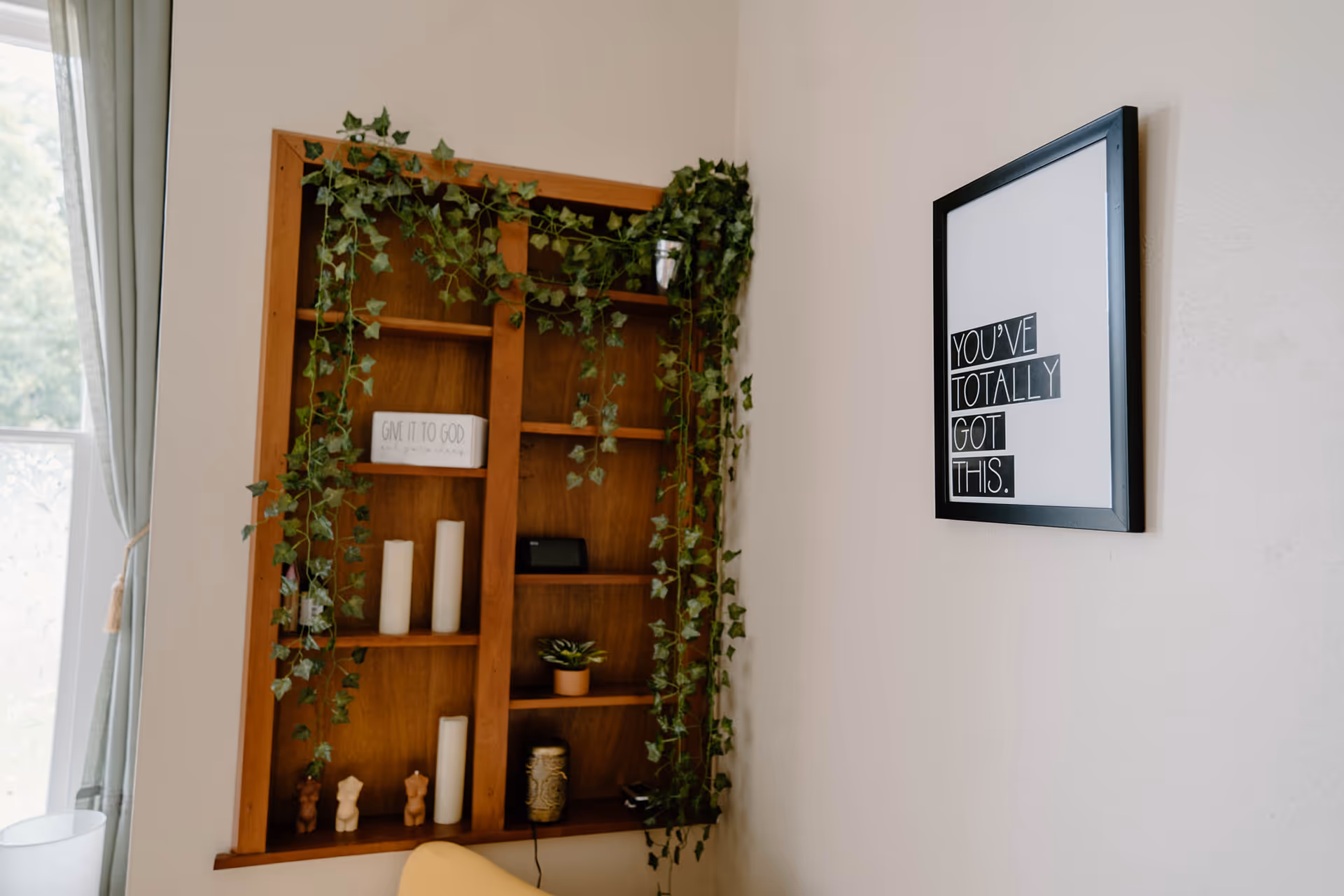 Wooden bookshelf with ivy, candles, and decor beside a framed inspirational quote.