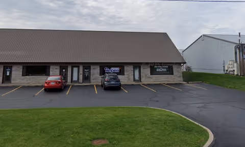 Front exterior of Senior Helpers facility: single-story stone building with brown metal roof.
