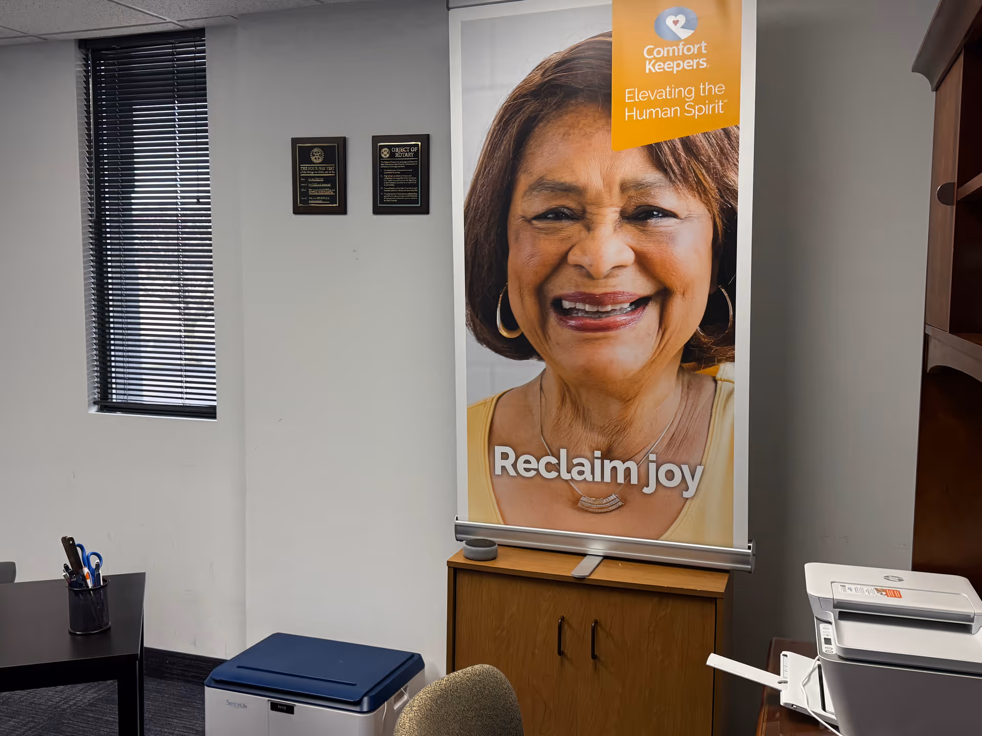 Interior office area with a Comfort Keepers banner showing a smiling woman and desk.