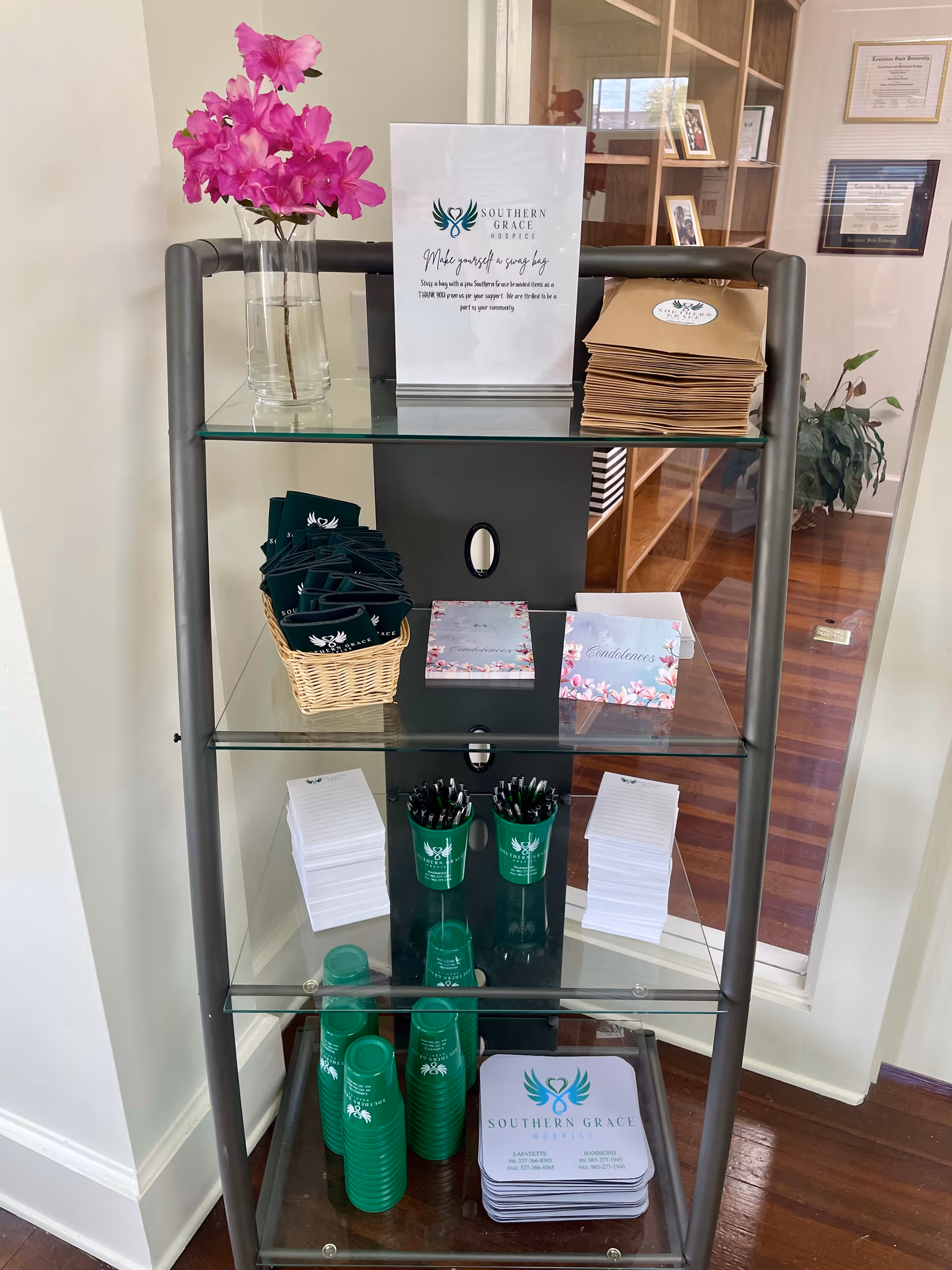 Glass shelving unit displaying pink flowers and hospice brochures in a lobby.
