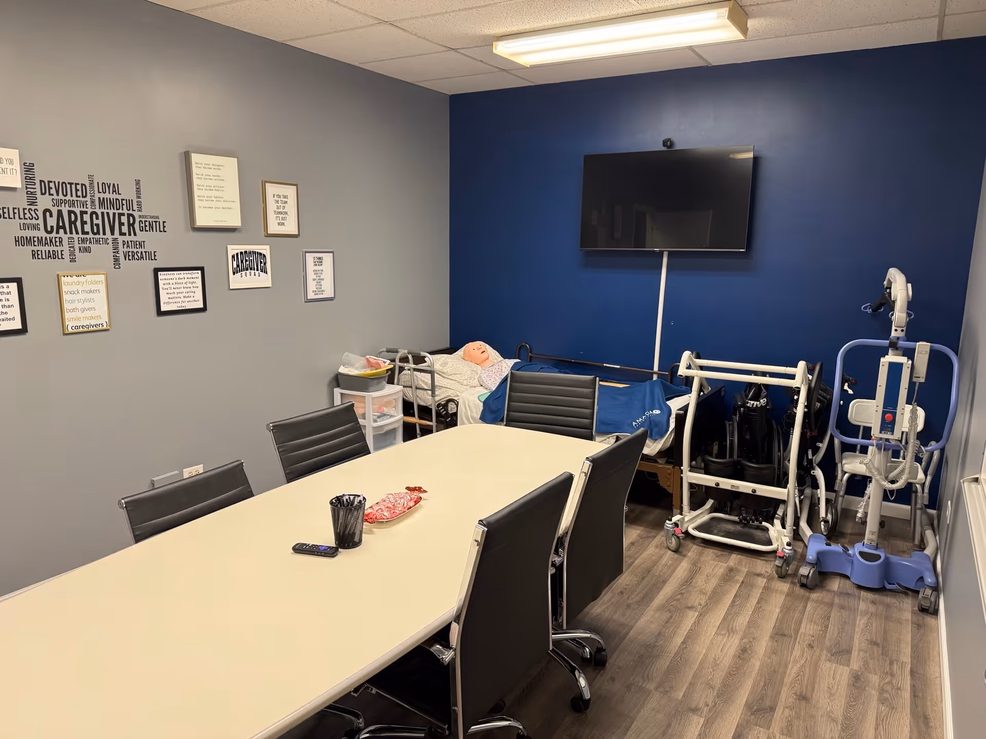 A conference-room interior featuring a long table, chairs, wall art, and visible medical equipment.