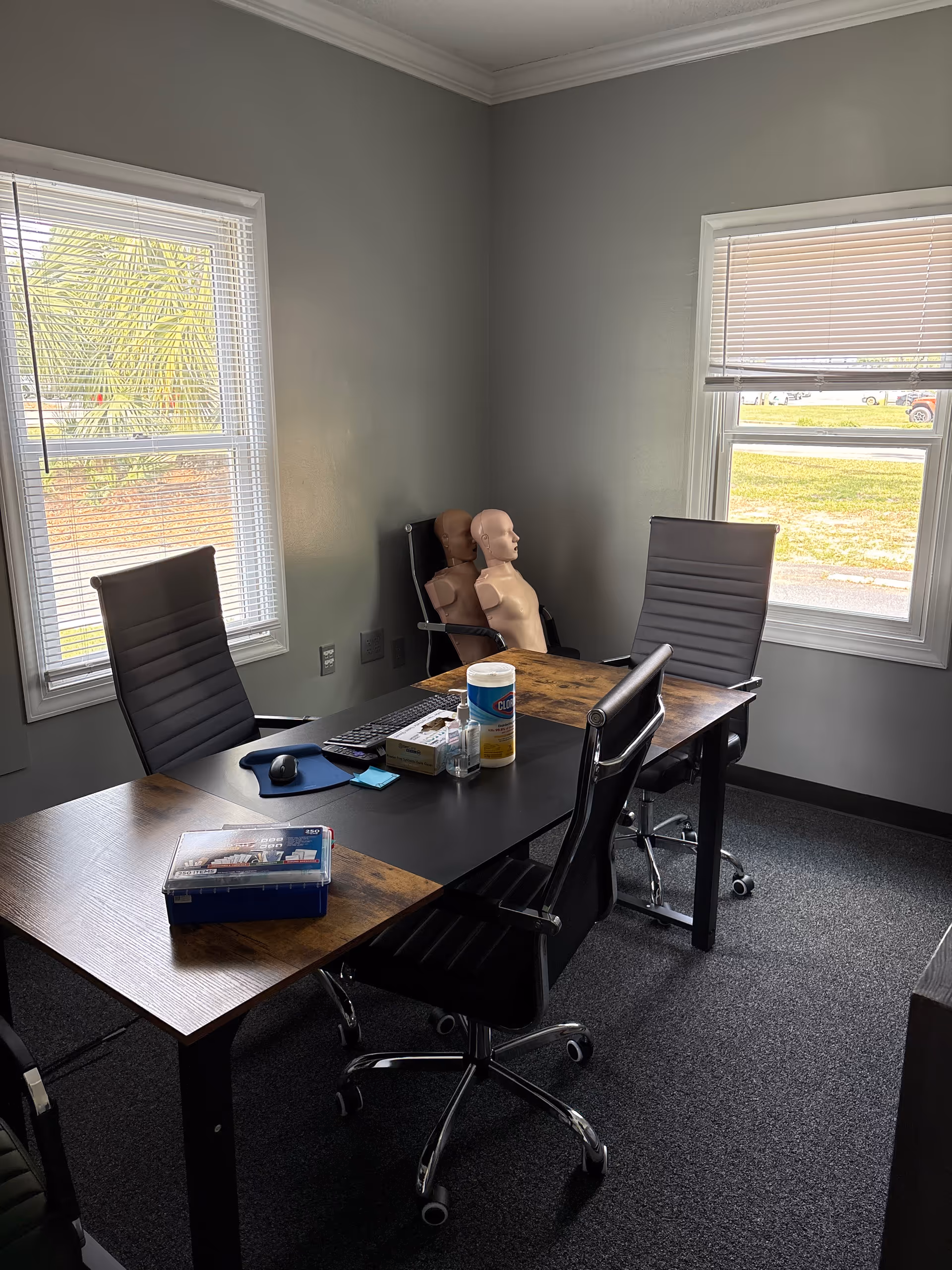 A conference room with a wooden table, black office chairs, and a medical training mannequin.