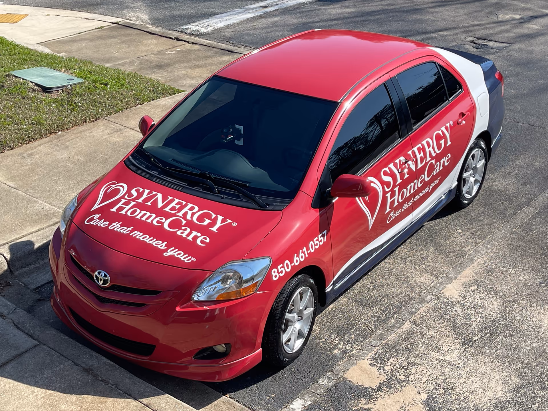Red Synergy HomeCare van parked on a street displaying logos and contact text.