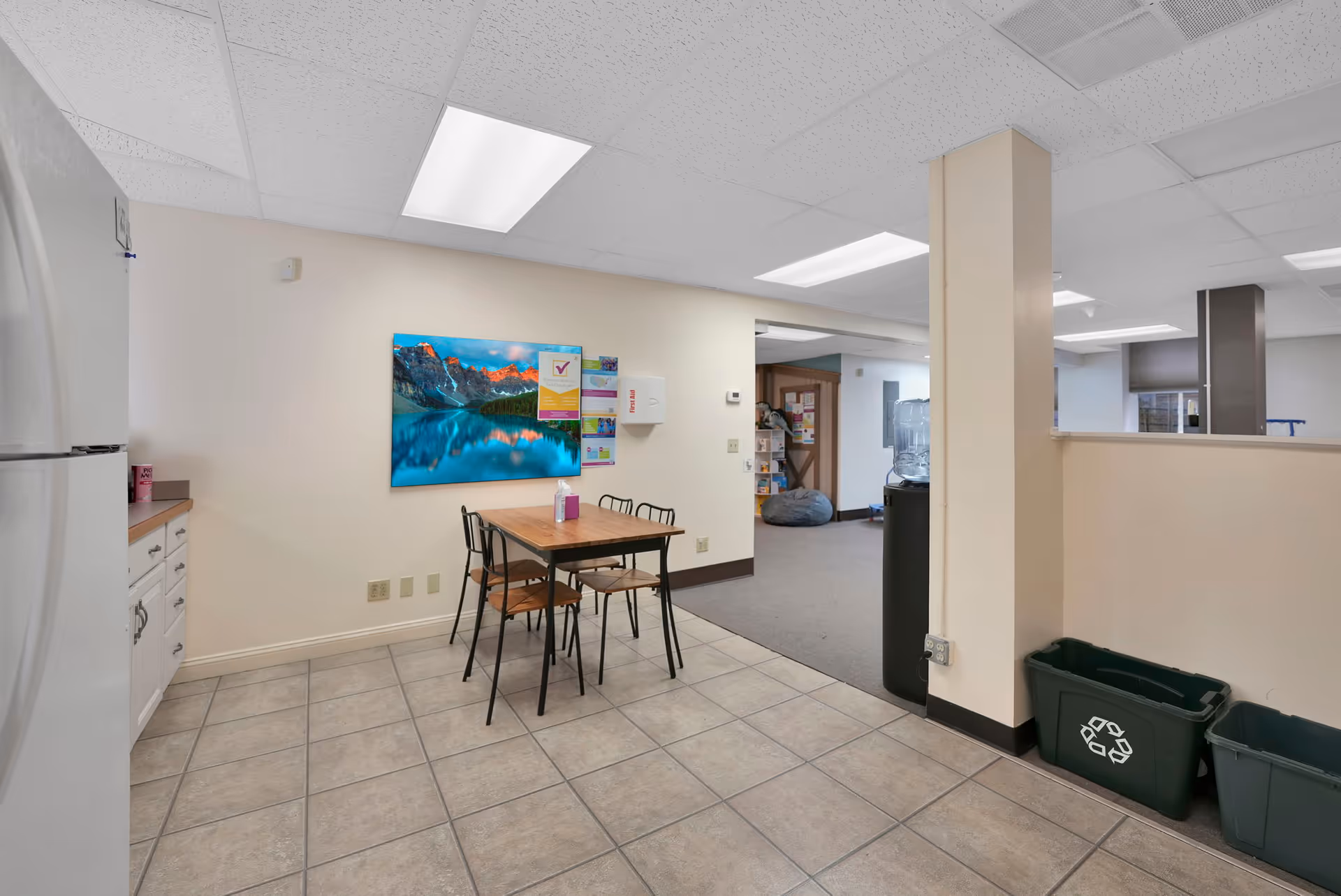 Interior common area with a small dining table, kitchenette, and hallway in a senior facility.