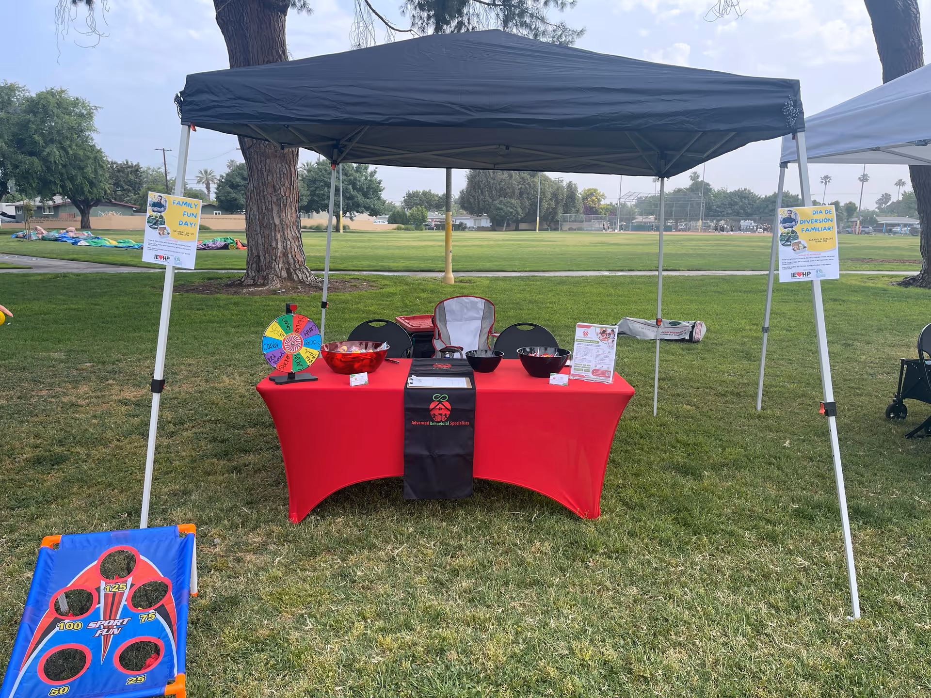 Outdoor event booth with a red table under a canopy and a spinning wheel