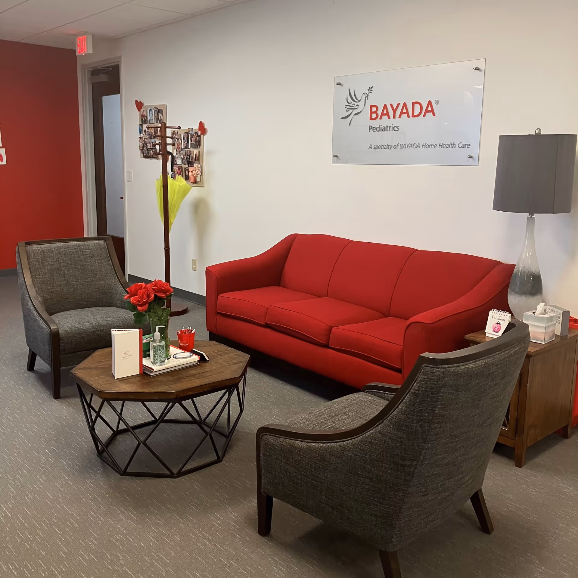 A modern clinic lounge with a red sofa, gray chairs, coffee table, and BAYADA Pediatrics sign.