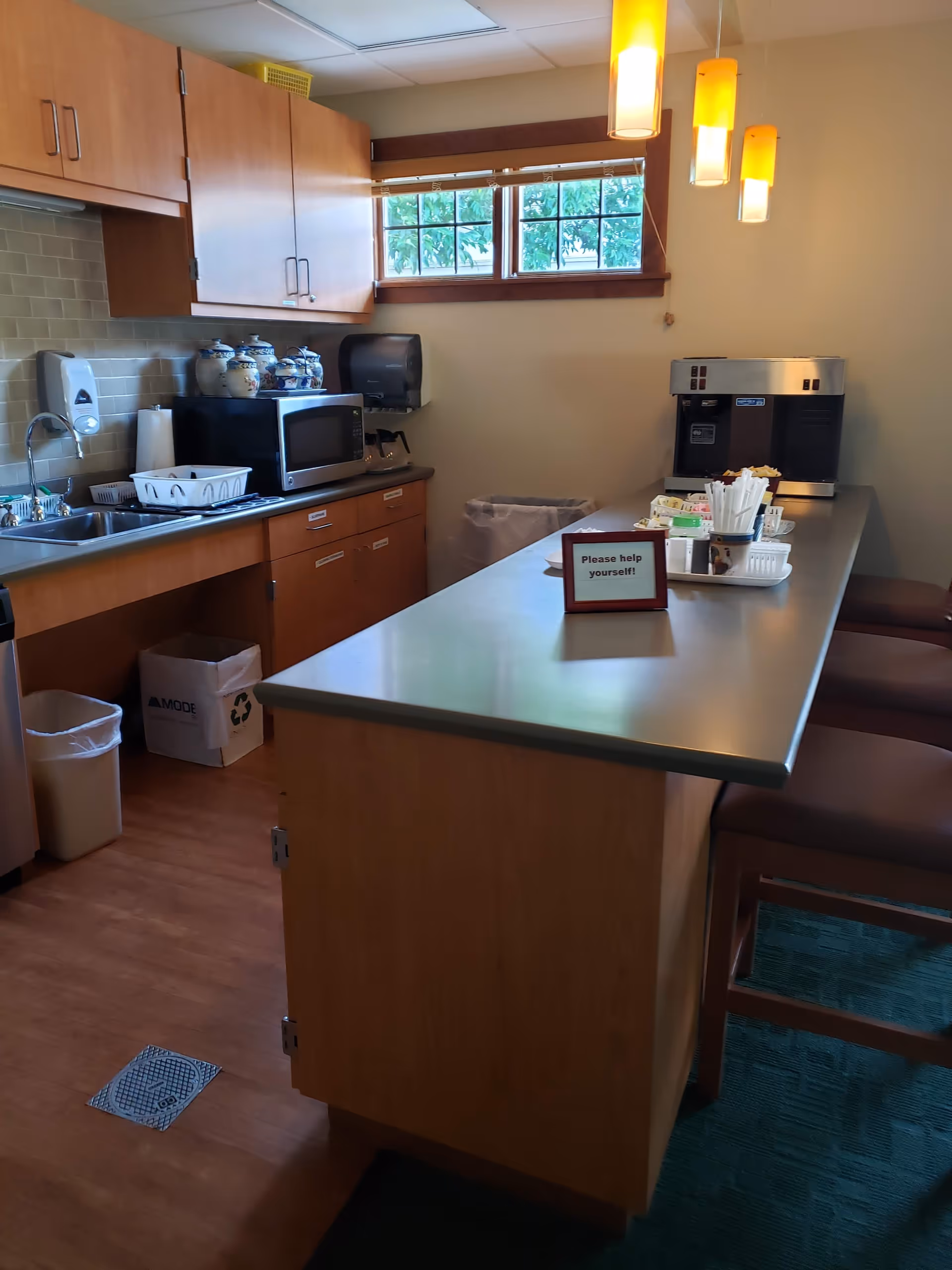 Long kitchenette with cabinets, sink, microwave, coffee machine, and a serving counter.