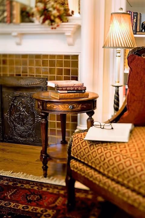 Cozy living room scene with a fireplace, side table, lamp, and upholstered chair.