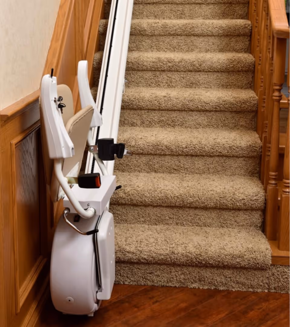 Indoor stair lift attached to carpeted stairs beside wooden railing and wall.