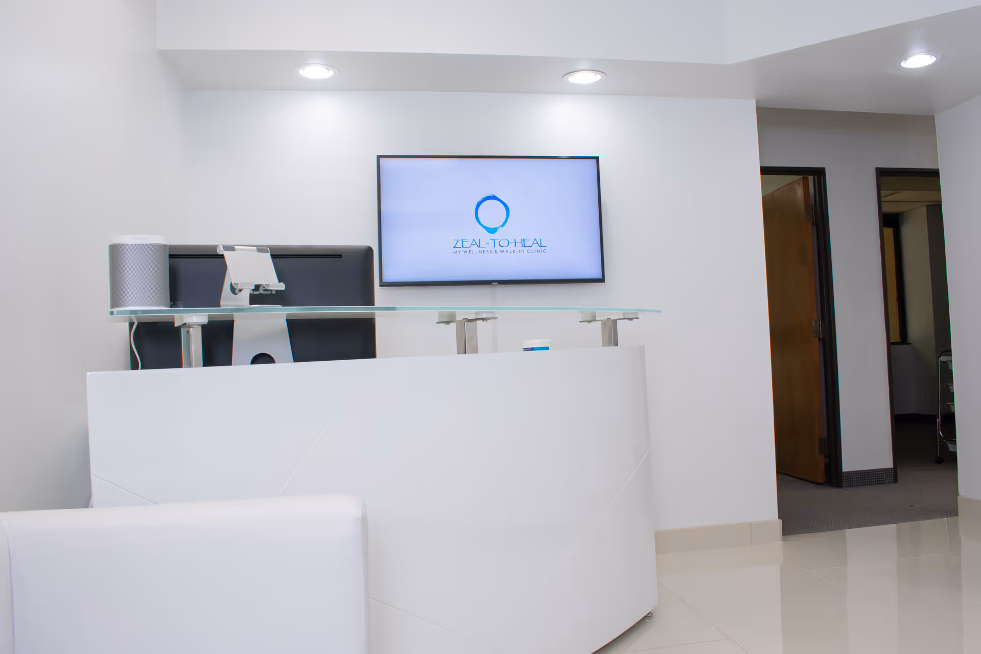 Modern clinic reception area featuring a white desk, wall TV, and doorway.