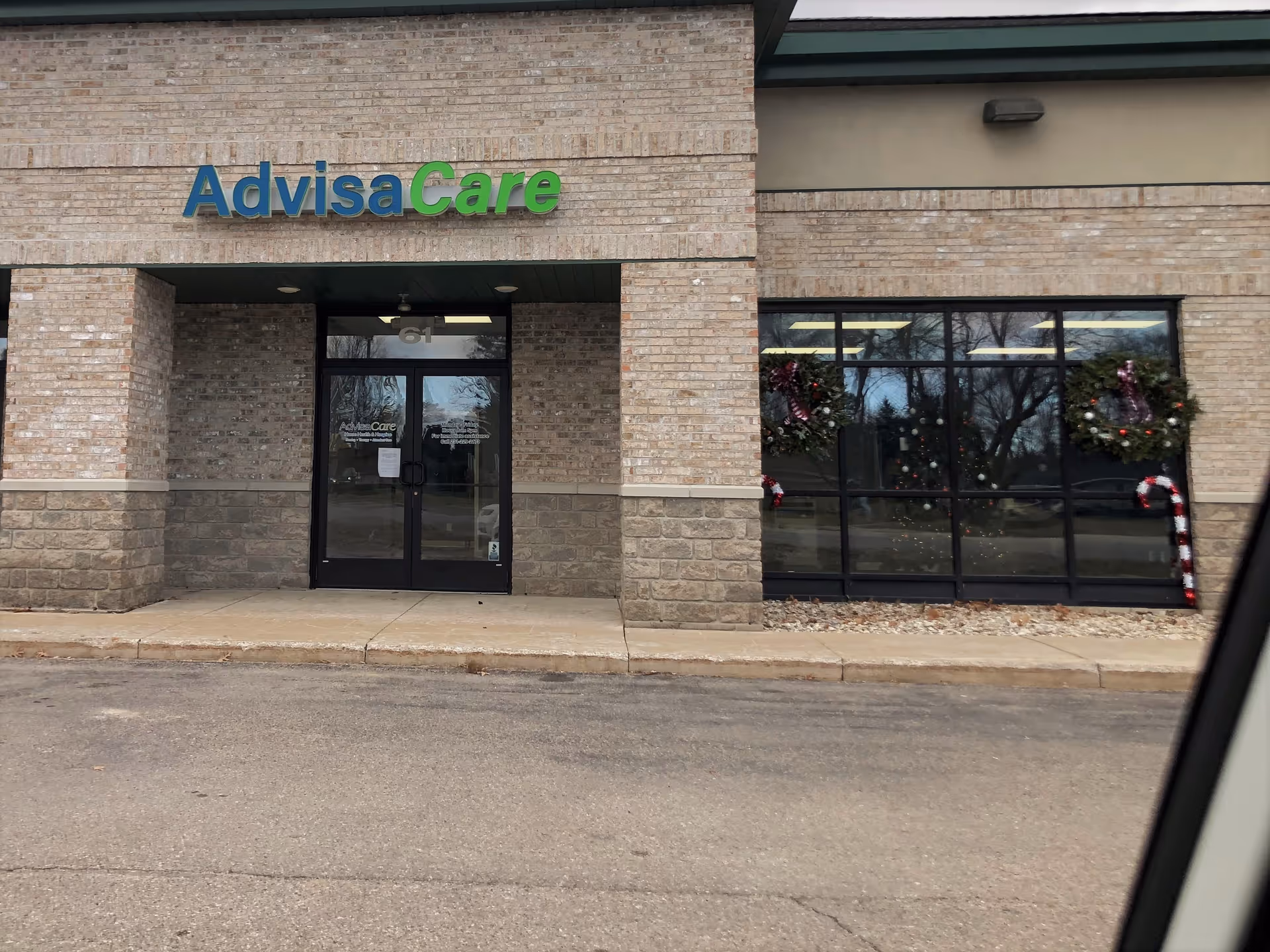 AdvisaCare storefront entrance with brick façade and holiday wreaths in large windows.