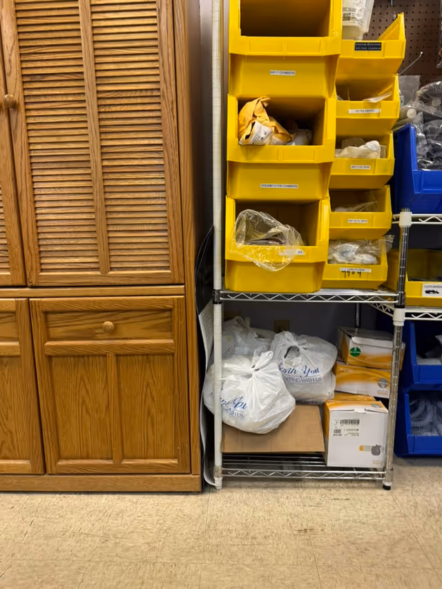 Wooden cabinets sit beside a metal shelving unit filled with yellow bins and bags.