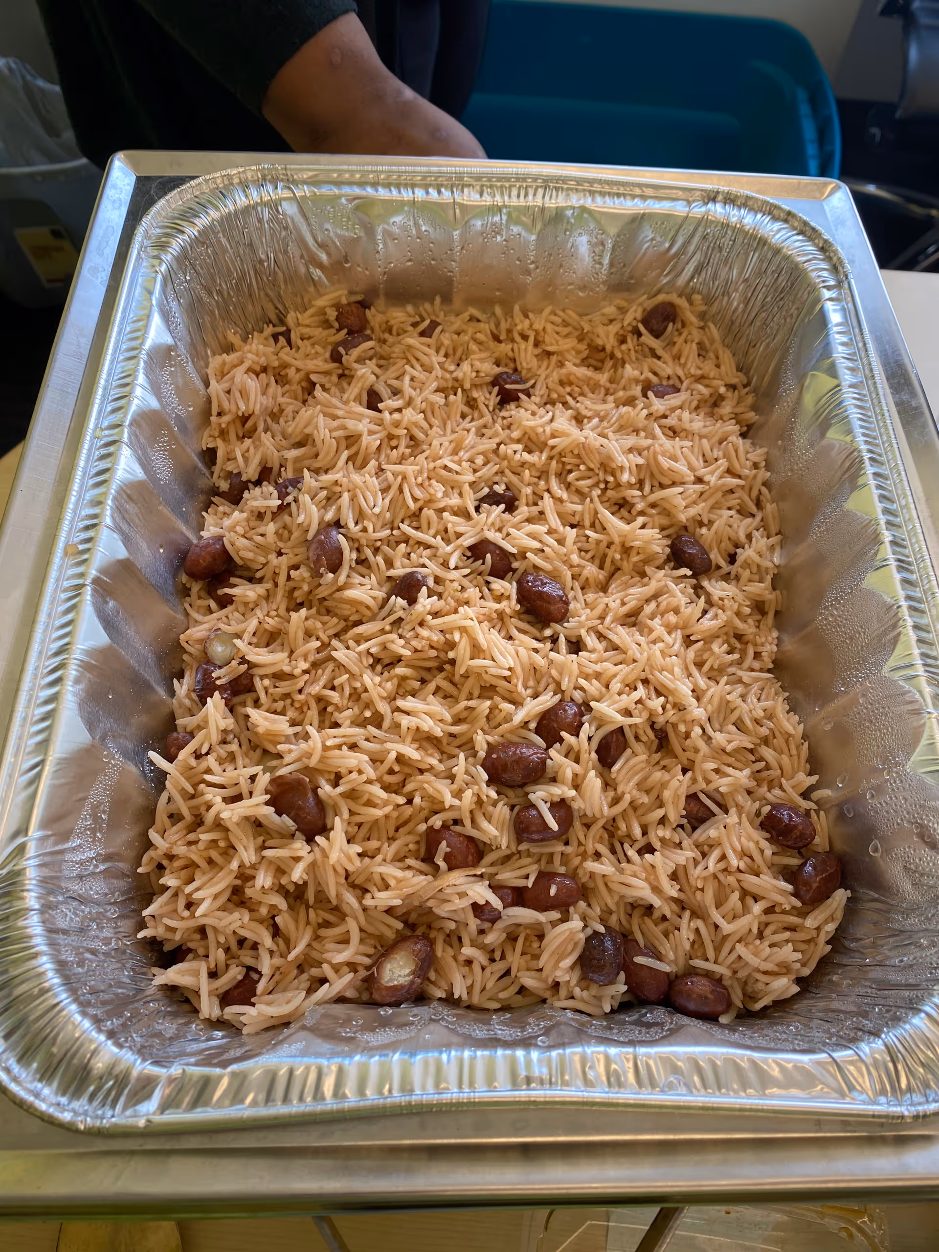 Large aluminum tray filled with seasoned rice and beans on a table in a dining area.