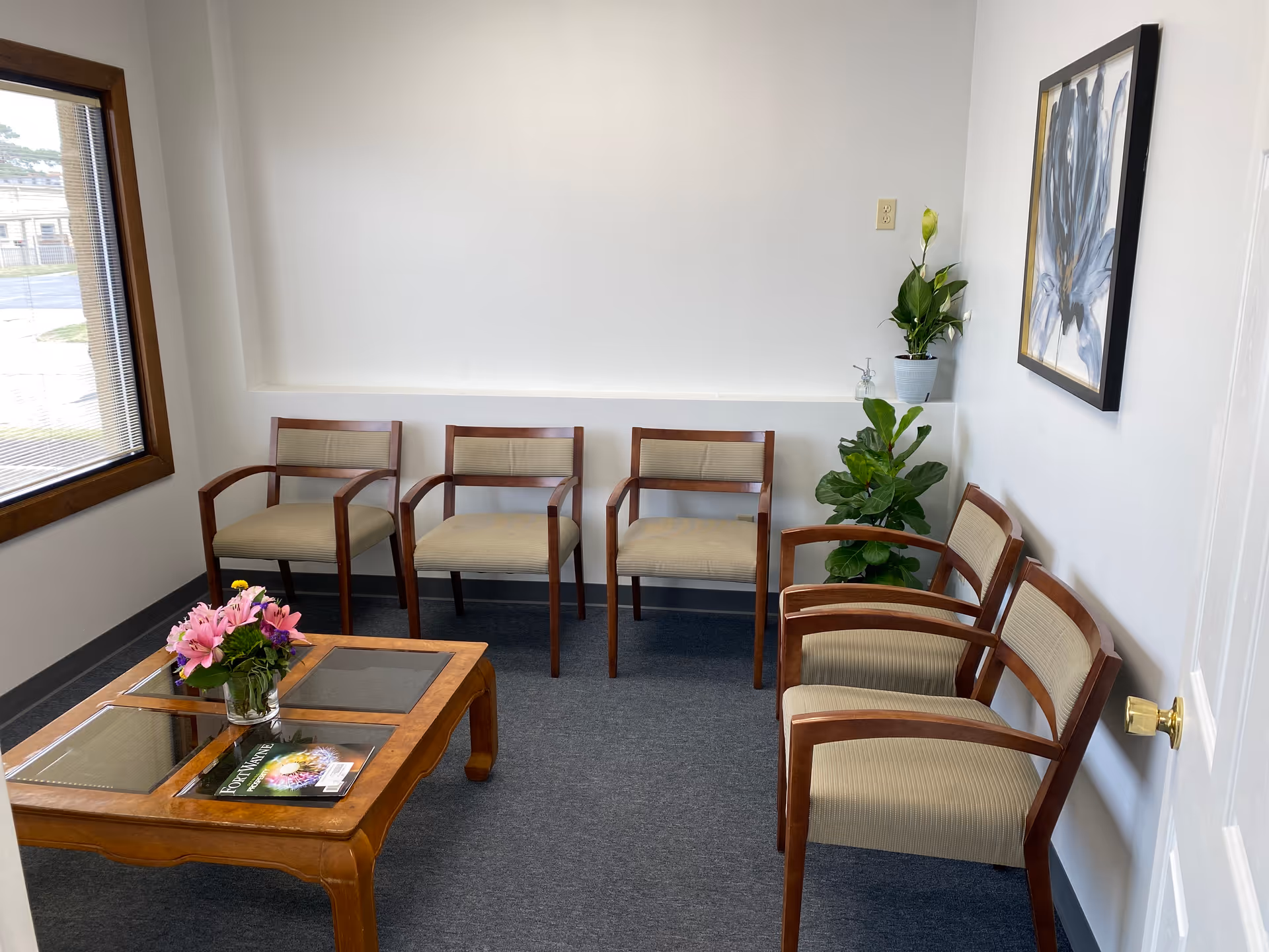 Small waiting area with wooden chairs, a coffee table, plants, and framed artwork.