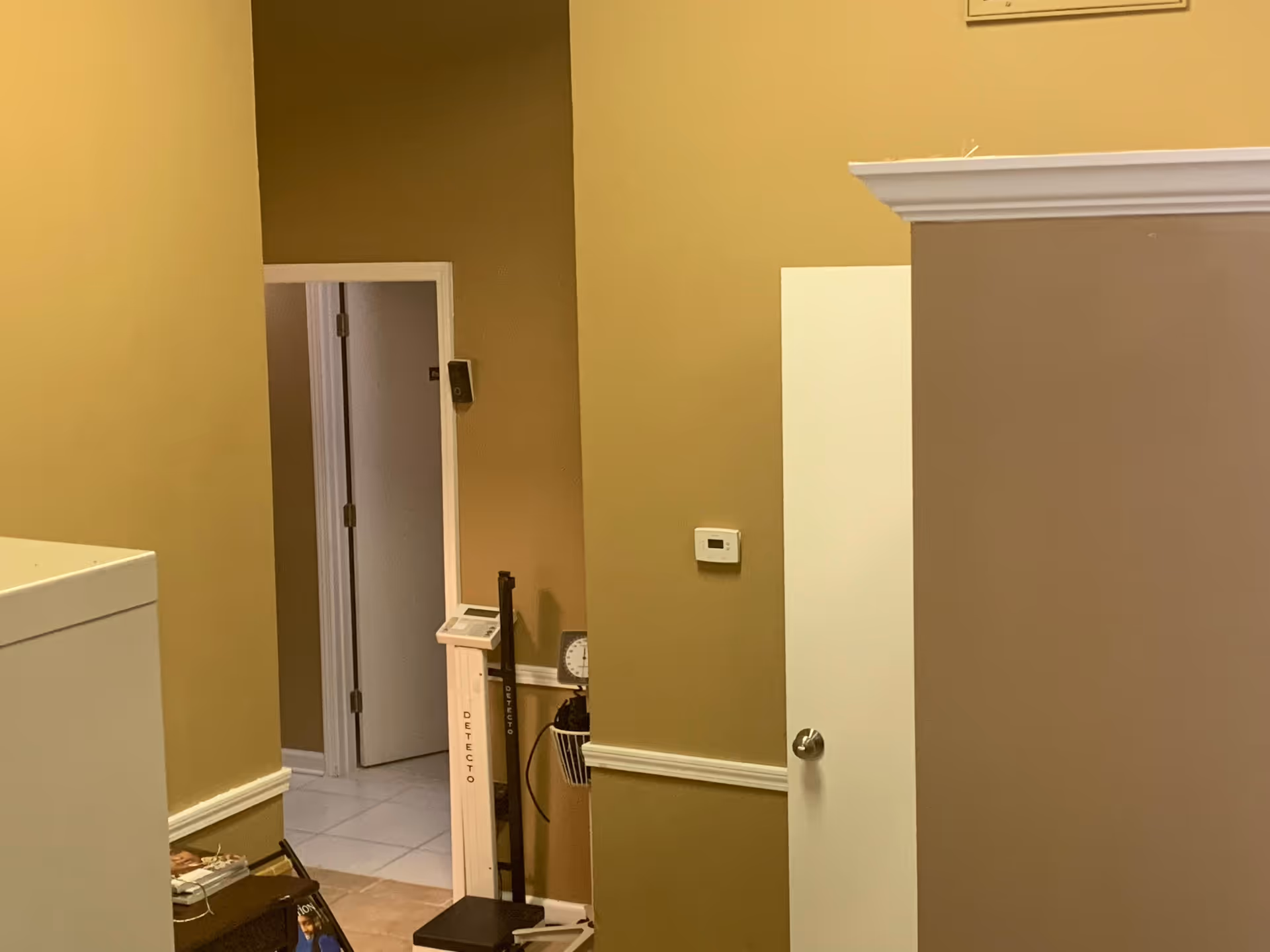 Interior hallway with beige walls, doorway, and a scale device in corner.