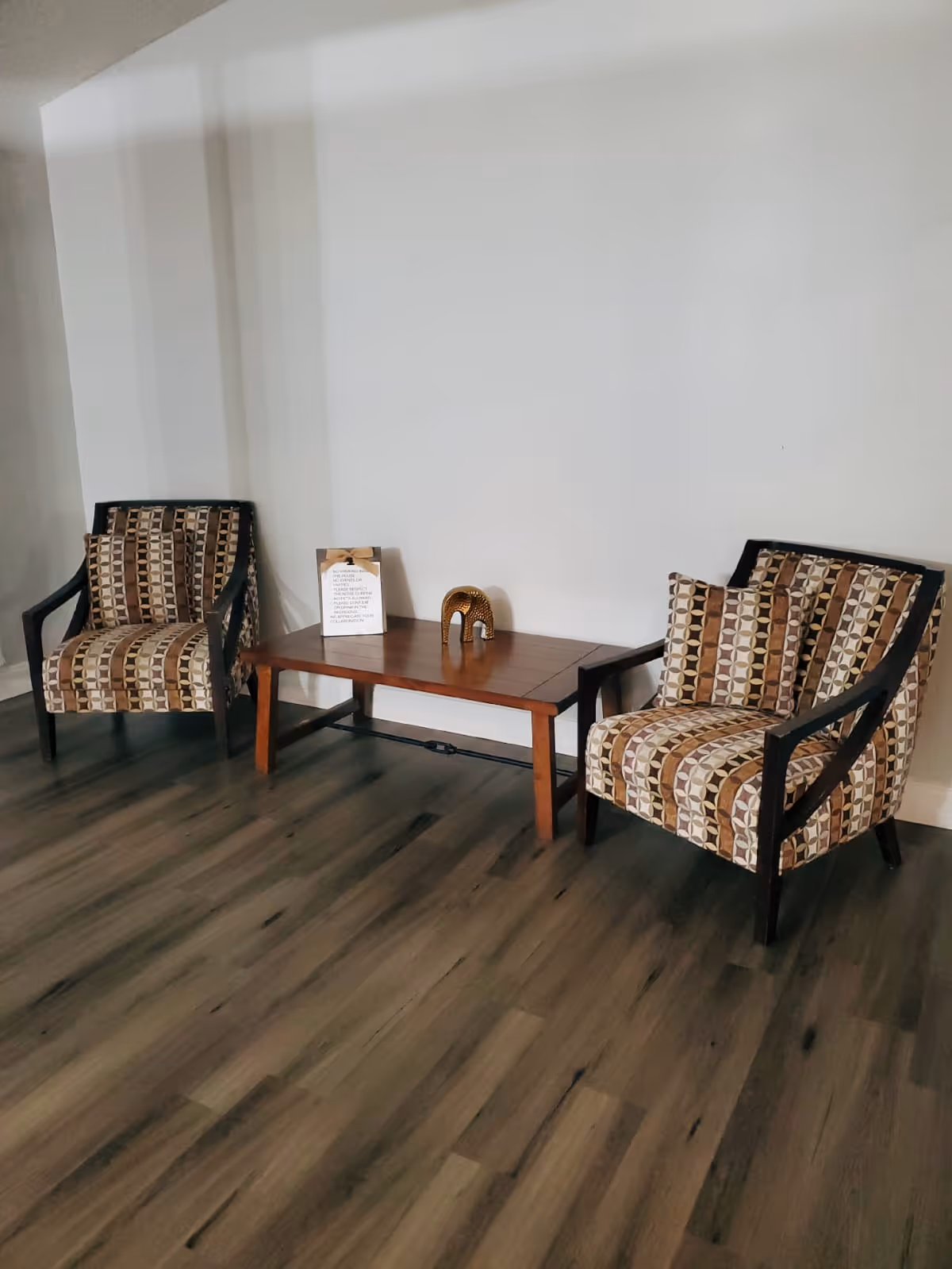 Two patterned armchairs flank a wooden table in a quiet lounge.