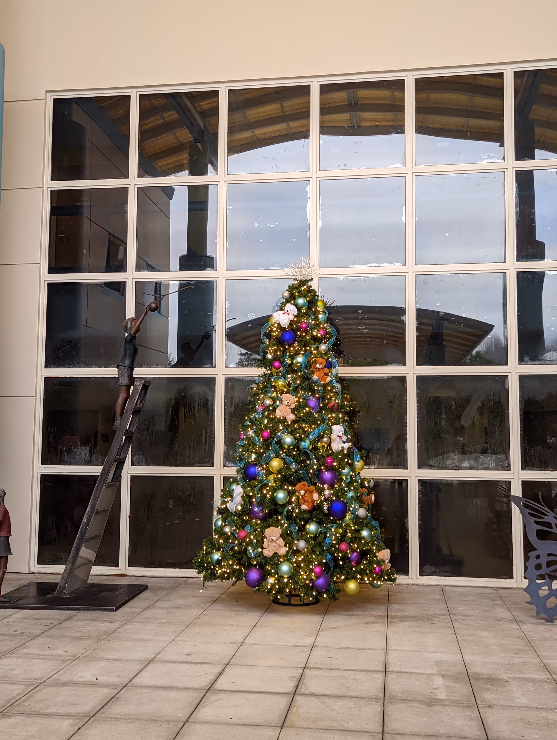 Inside a large lobby, a decorated Christmas tree stands beside grid windows.