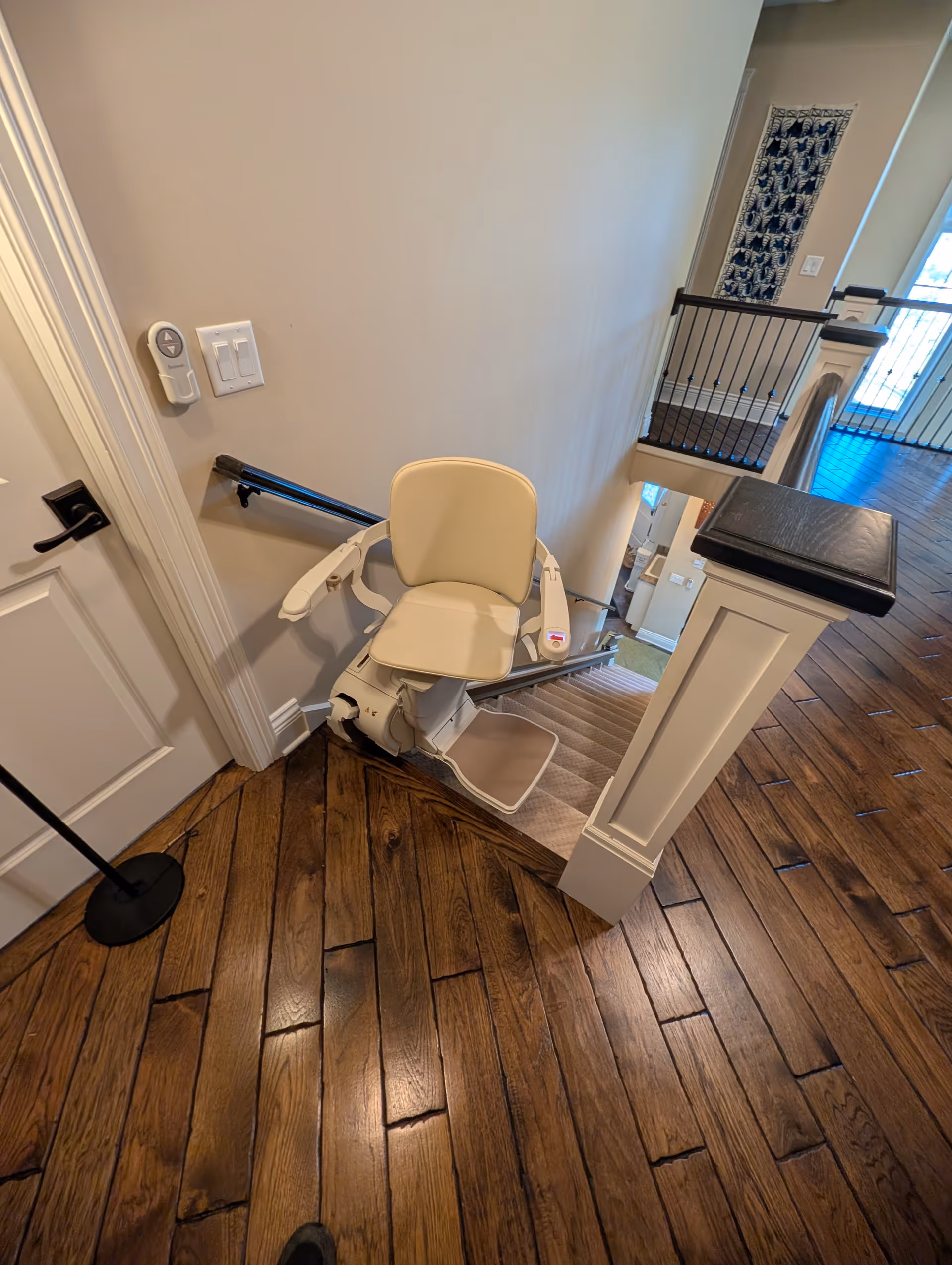 Interior stairwell with a cream stair lift chair, wooden floor, and railing.