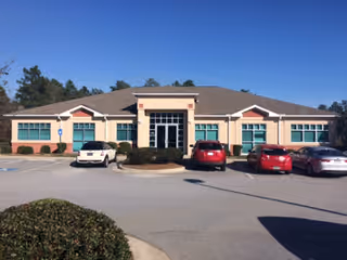A single-story building with beige exterior, turquoise trim, and cars parked in front.