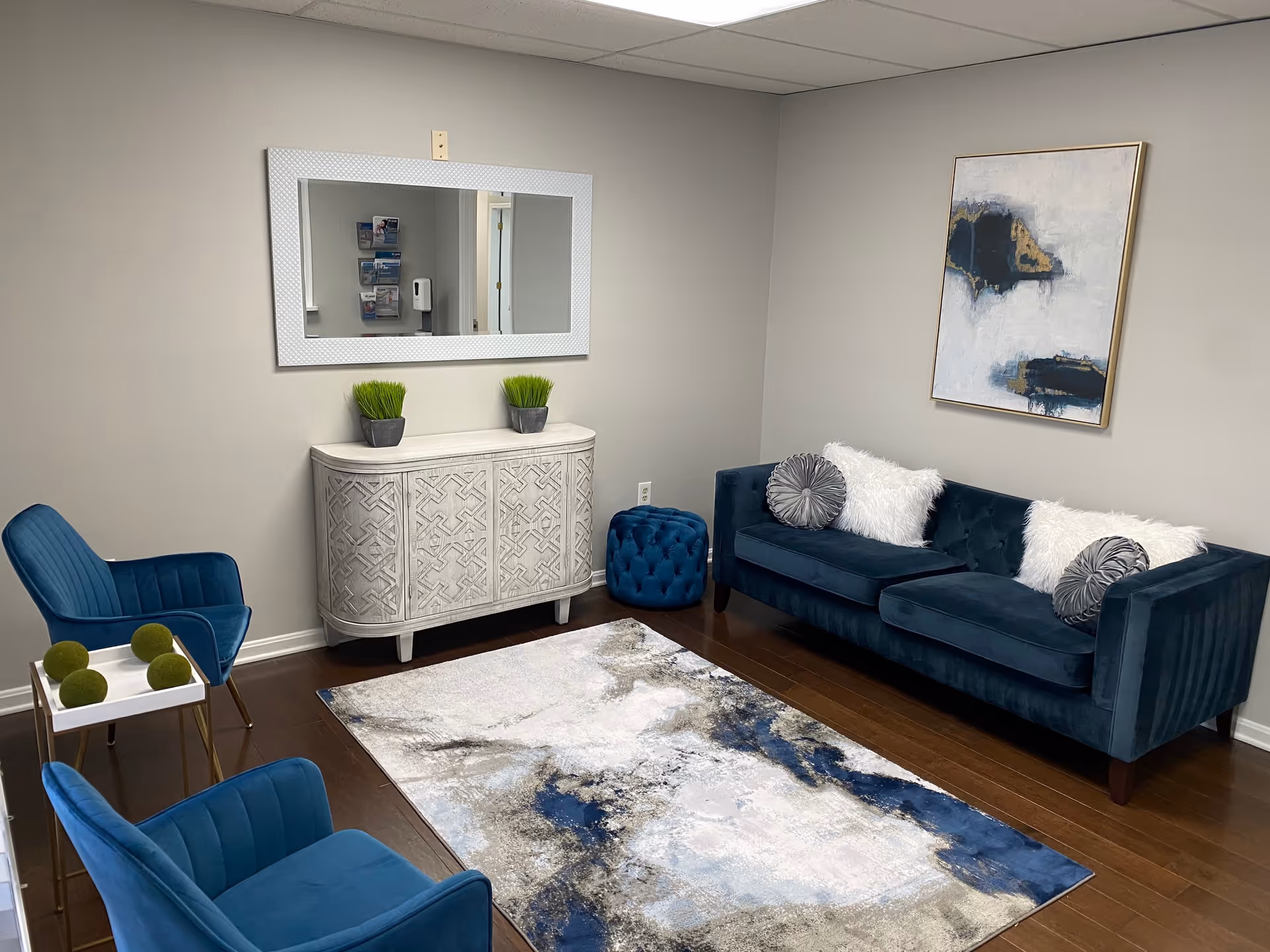 Cozy blue lounge area with sofa, chairs, rug, wall art, and cabinet in a modern lobby.