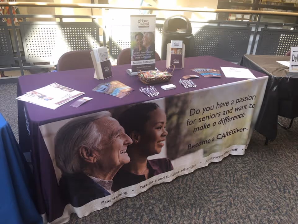 Promotional table draped in purple with caregiver recruitment materials at an indoor event.
