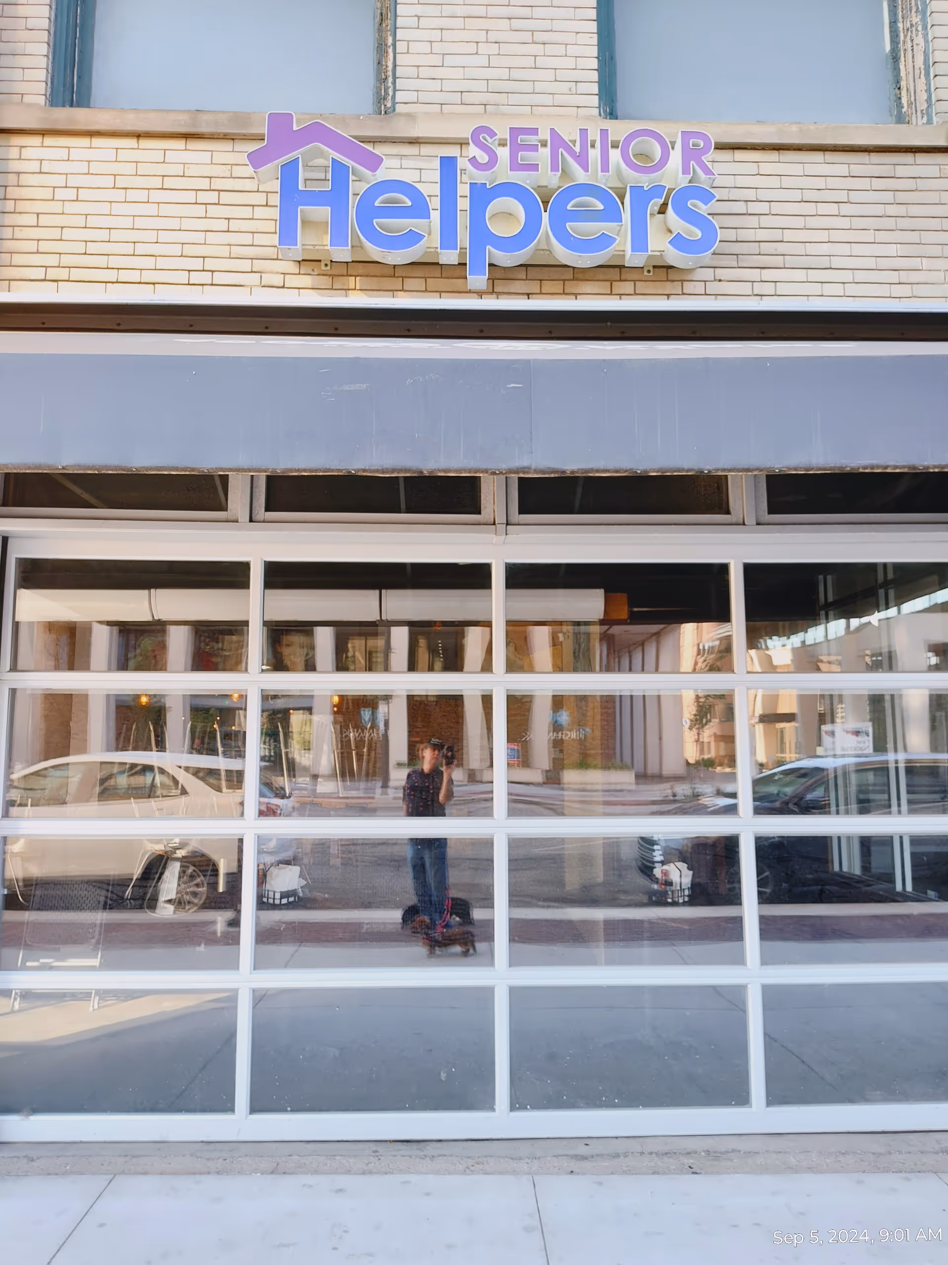 The facade of a Senior Helpers storefront features large glass windows and street reflections.