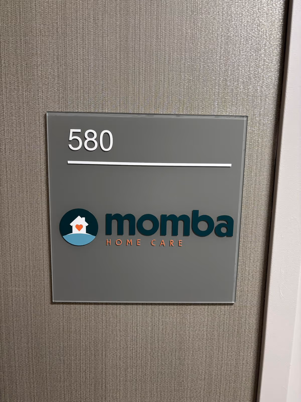 Gray wall sign displaying 580 and the Momba Home Care logo.