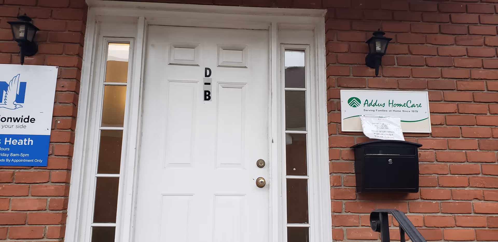 Brick exterior with white front door, sidelights, a black mailbox, lantern lights, and Addus HomeCare sign.