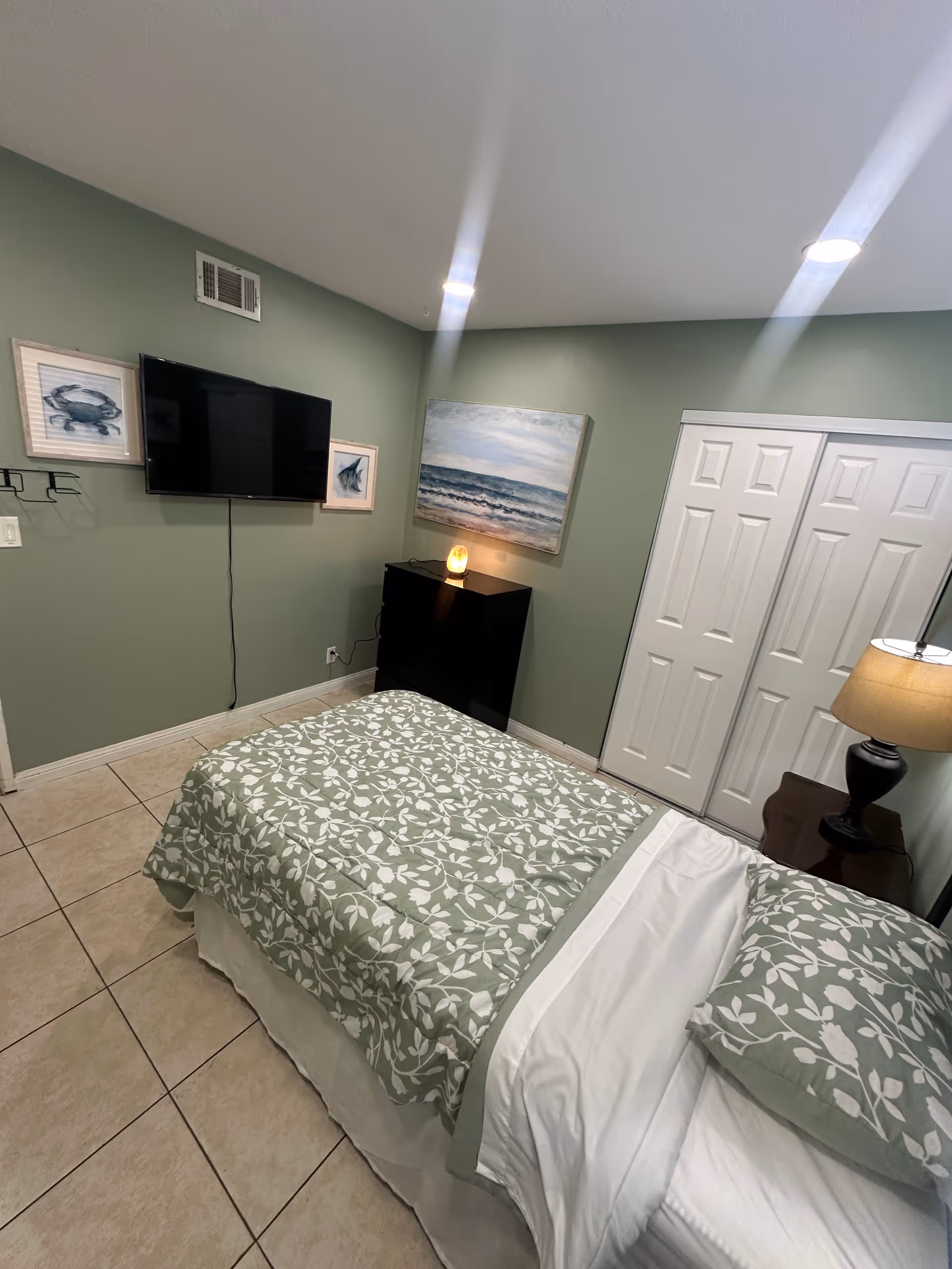 A cozy bedroom with a green patterned bedspread, TV, and nightstand.