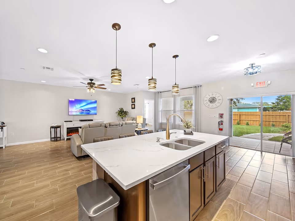 Spacious open living area with kitchen island, seating, TV, and sliding glass door.