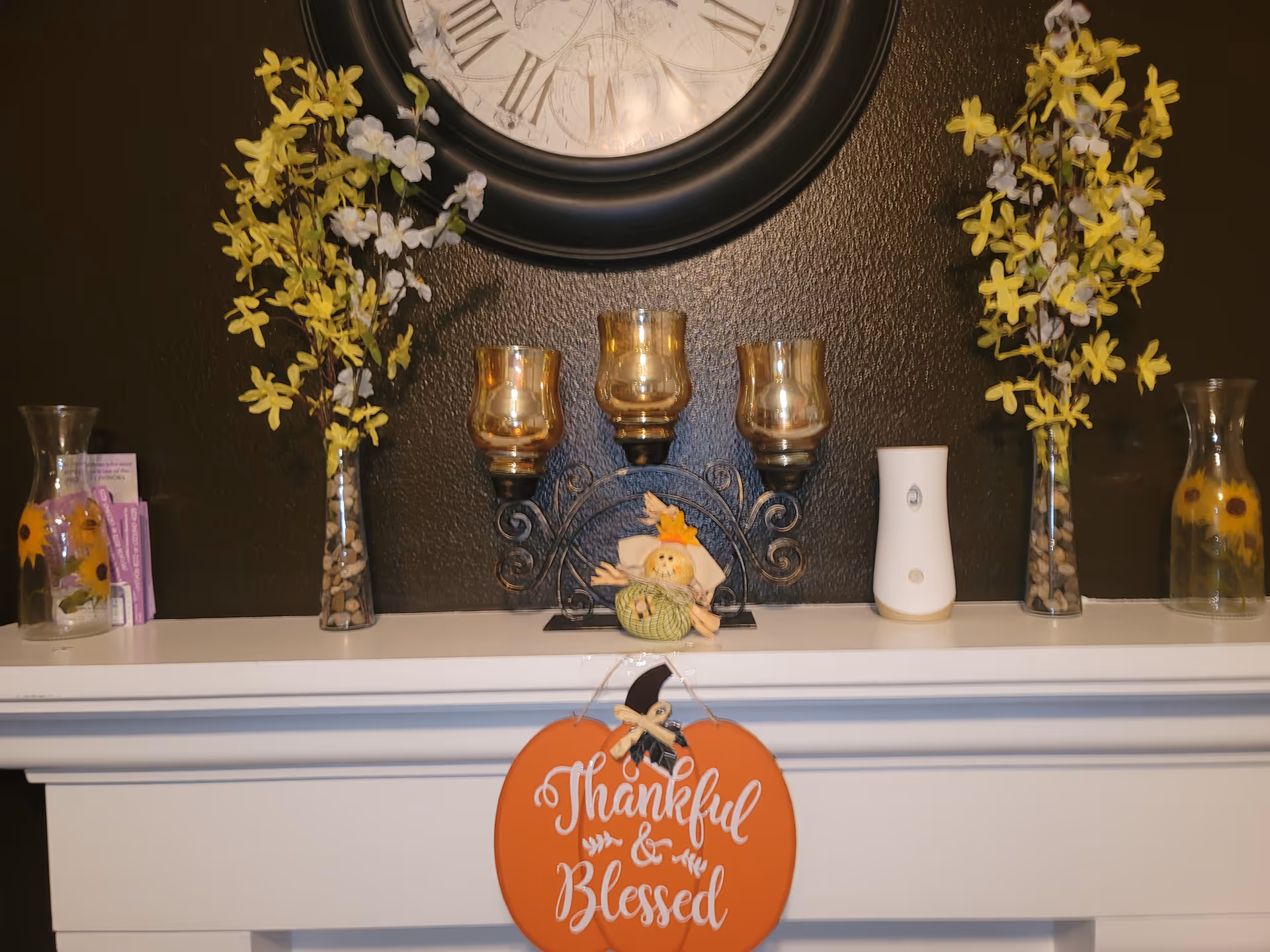 Decorative fireplace mantel features a clock, candles, vases, and a Thankful & Blessed sign.
