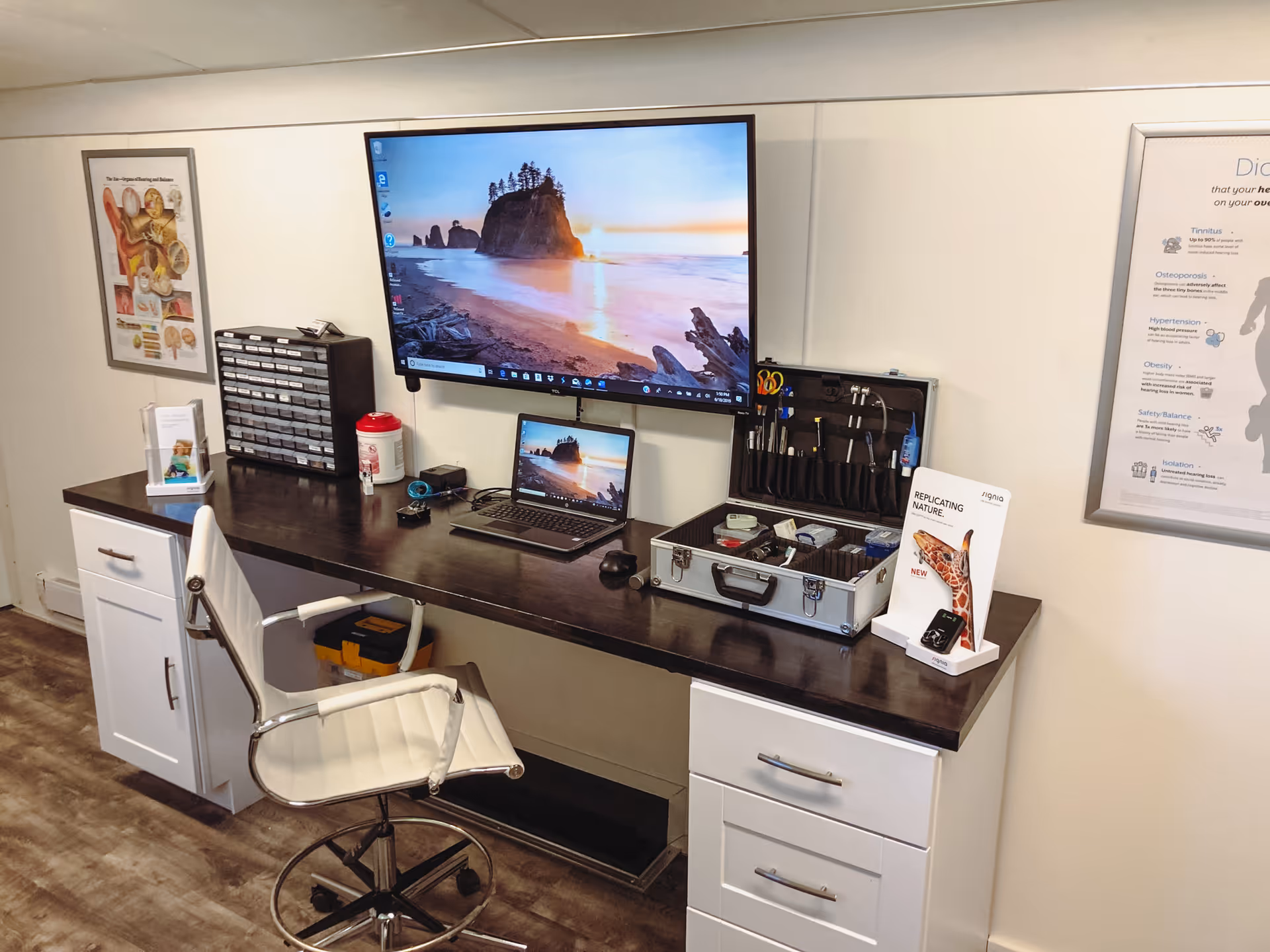 A dark wood desk with multiple monitors and a tool kit in a clinical hearing center.