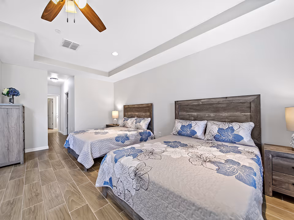 Two queen beds with blue floral quilts in a bright, modern bedroom.