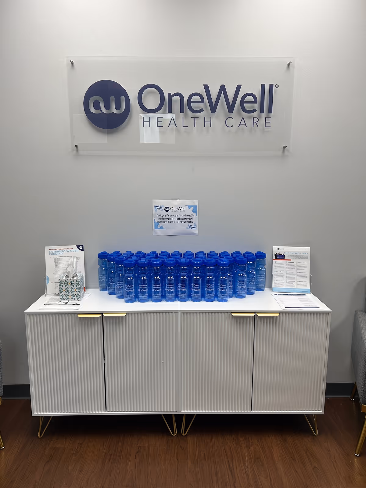 Lobby area with OneWell Health Care sign and a cabinet stocked with blue water bottles.
