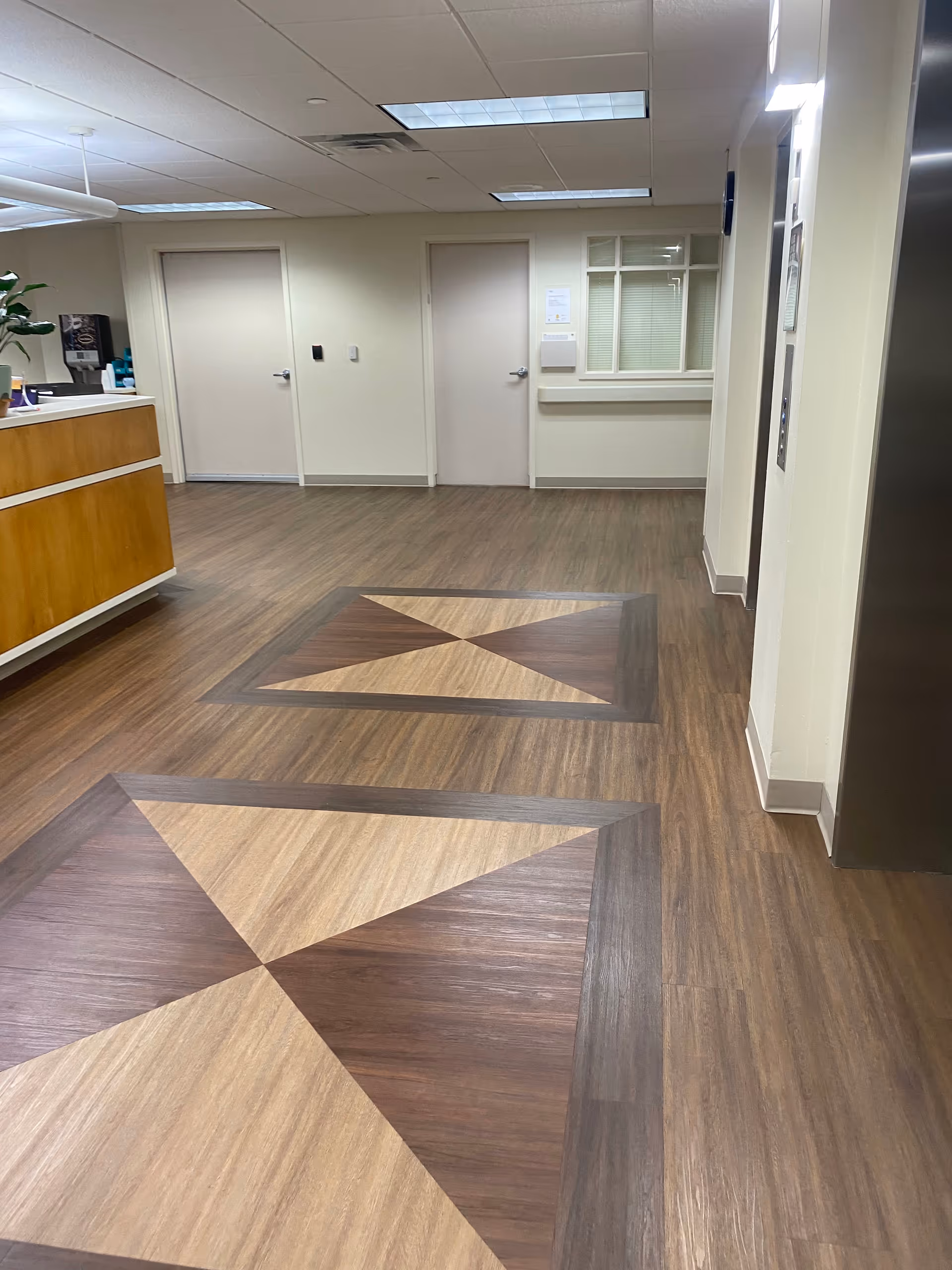 Interior lobby area with a geometric wood floor pattern and doors along the back wall.