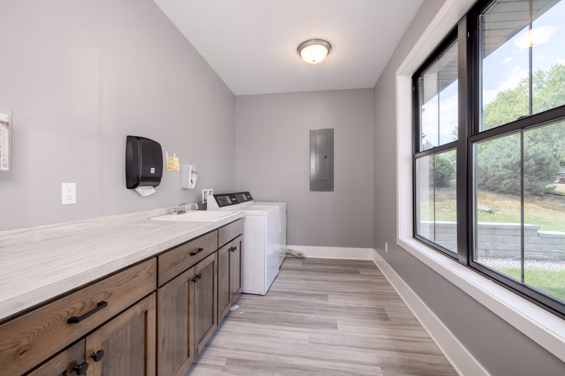 Clean laundry room with wooden cabinets, countertop, washer and dryer, and large window.