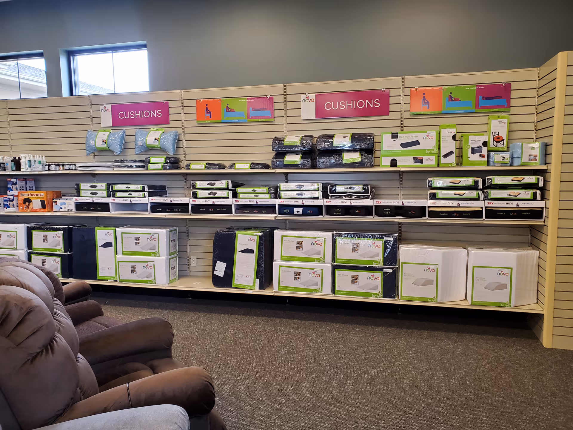 A showroom aisle with shelves of cushions, bedding, and medical supplies, plus brown recliner chairs.