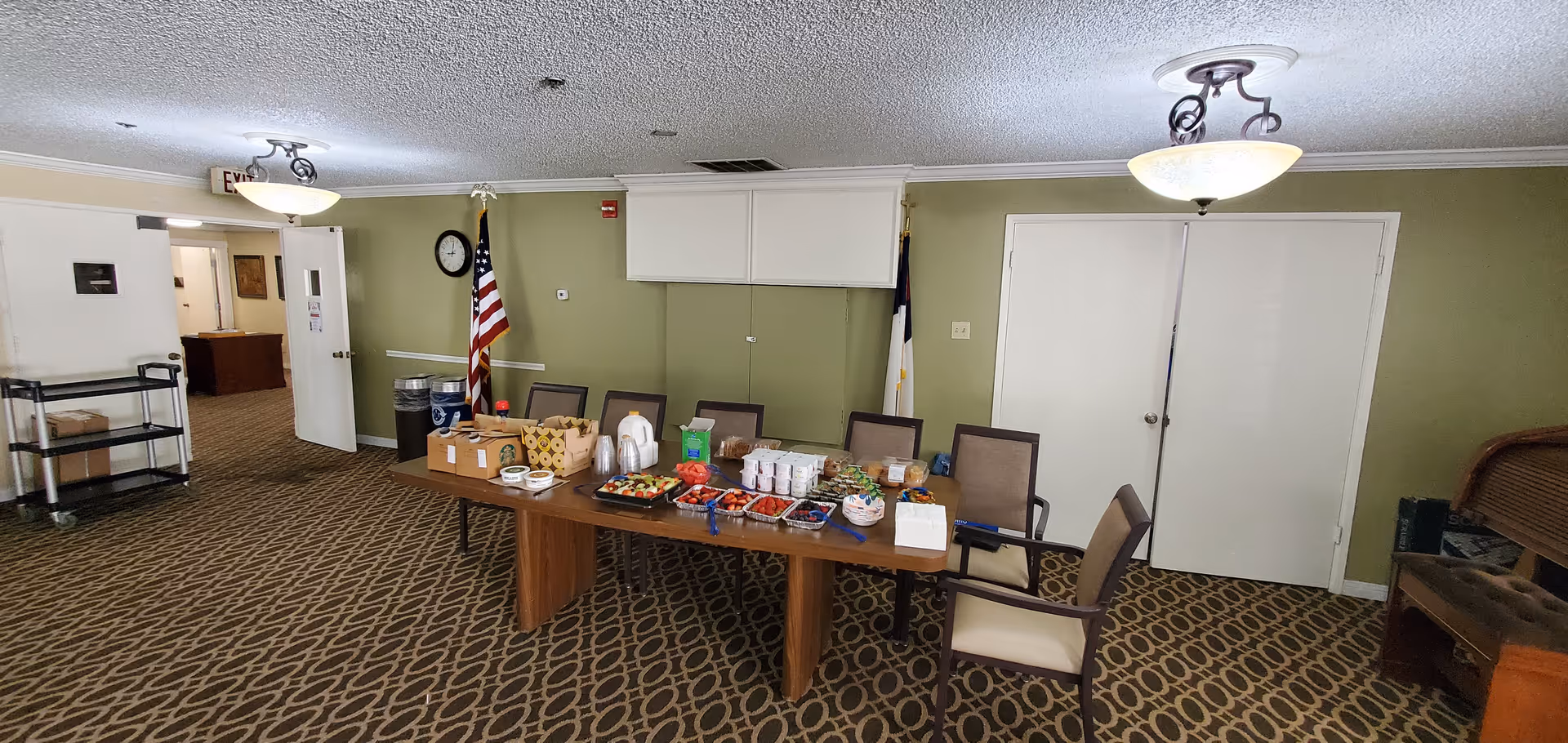 Interior dining room with long snack table, chairs, two flags, and green walls.