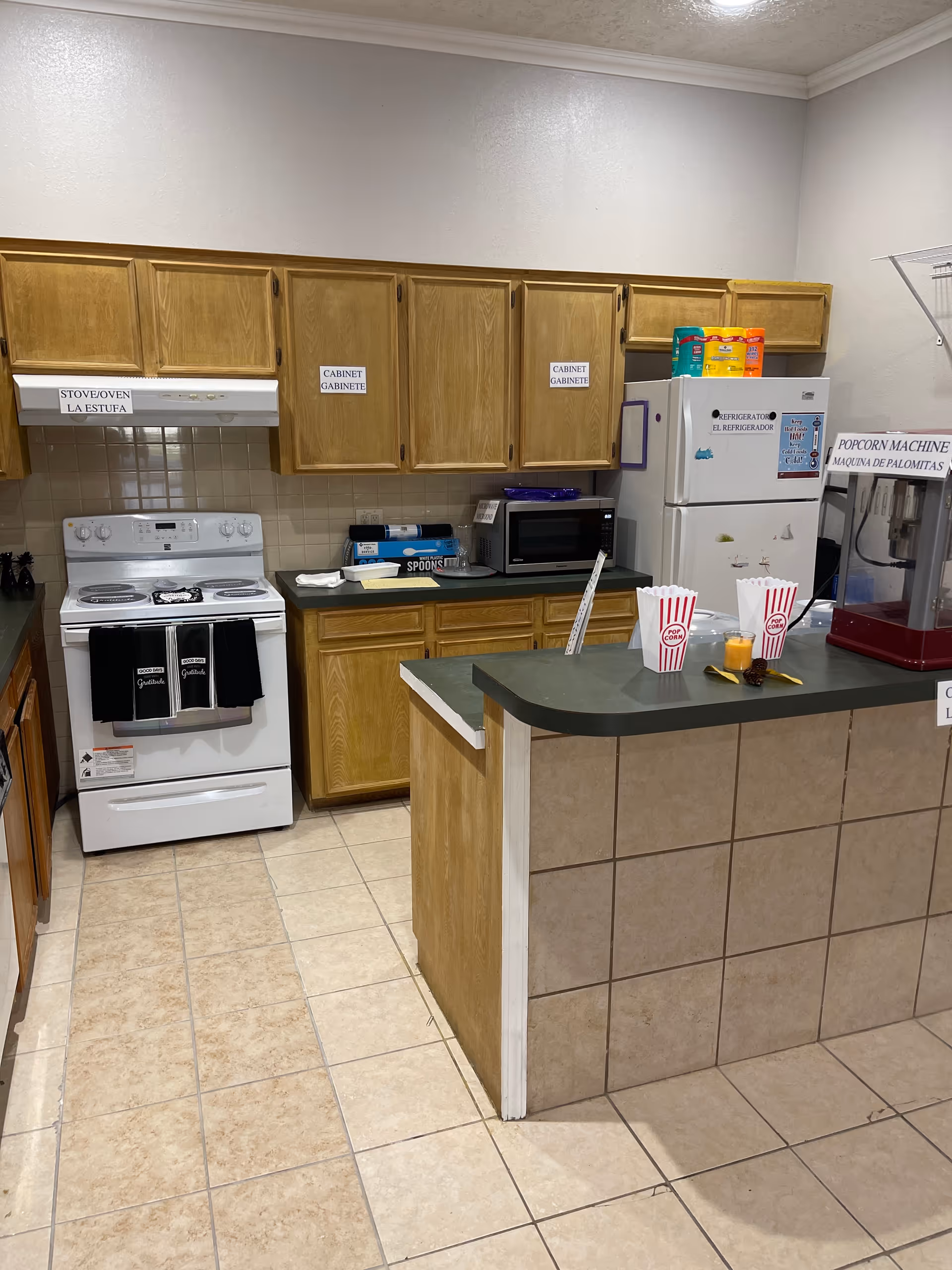 Kitchen area with wooden cabinets, stove, microwave, refrigerator, and popcorn machine.