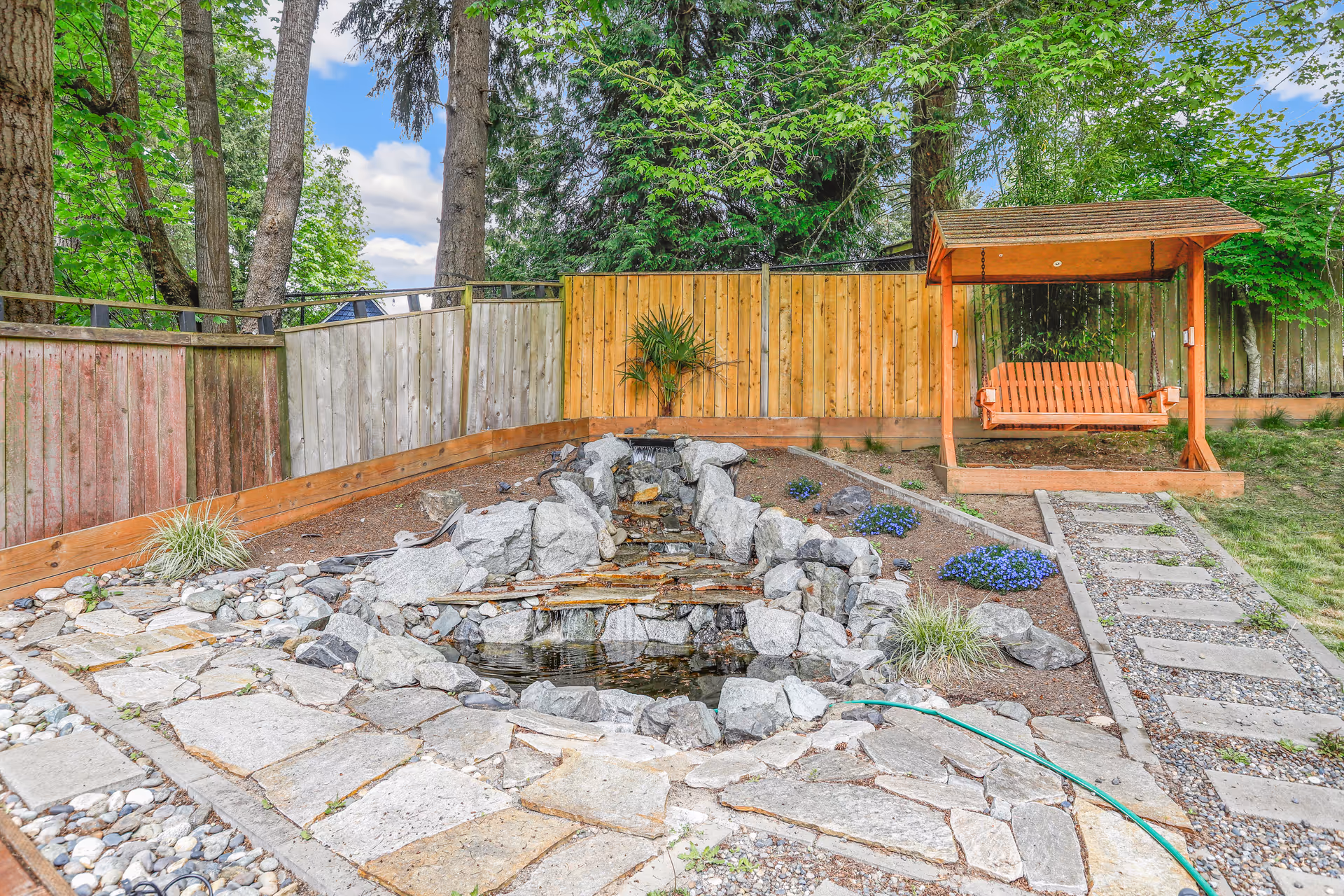 Fenced backyard with rock pond, stone path, and wooden swing.