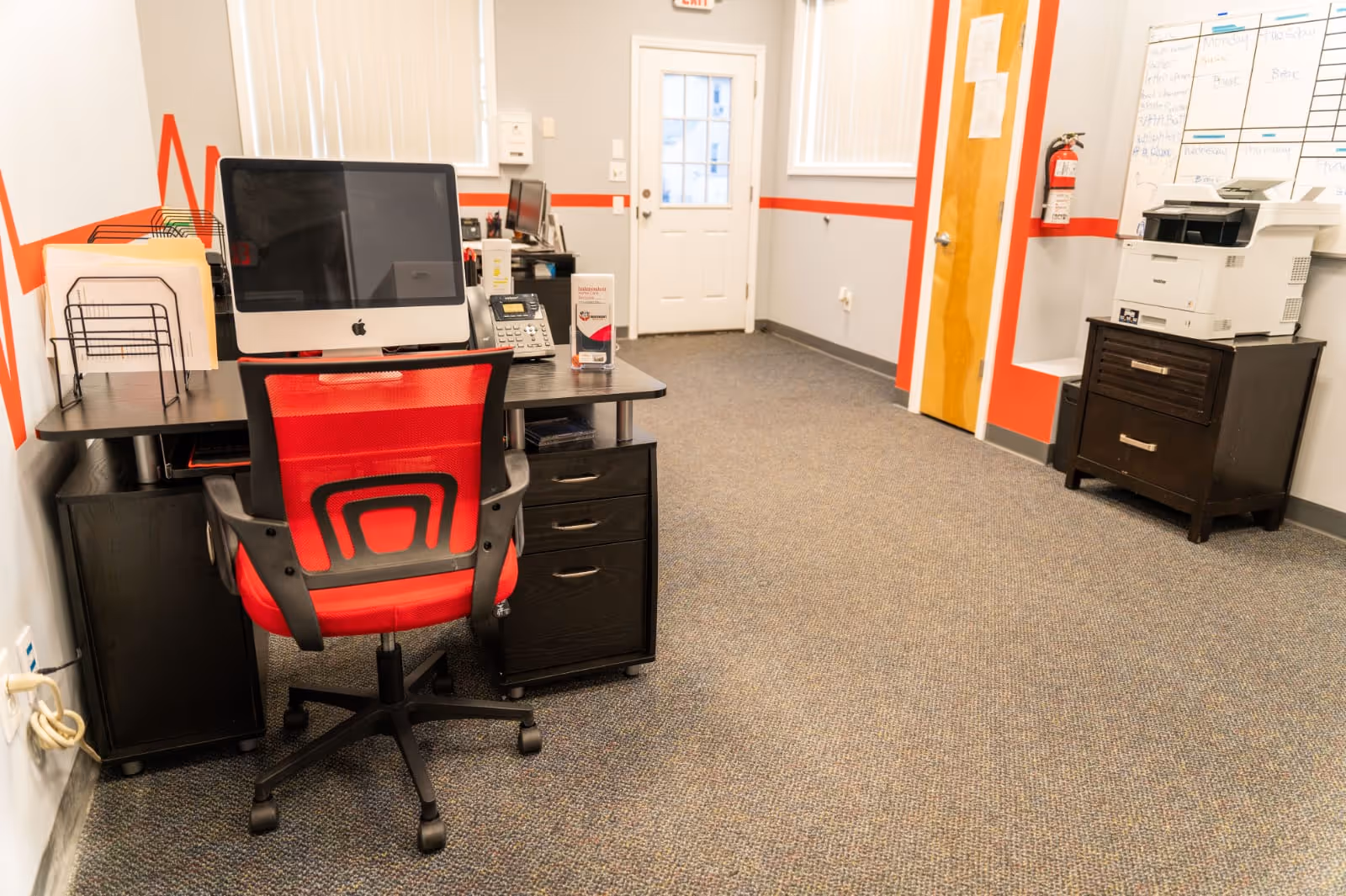 Office workspace in a senior care facility with computer, red chair, and copier.
